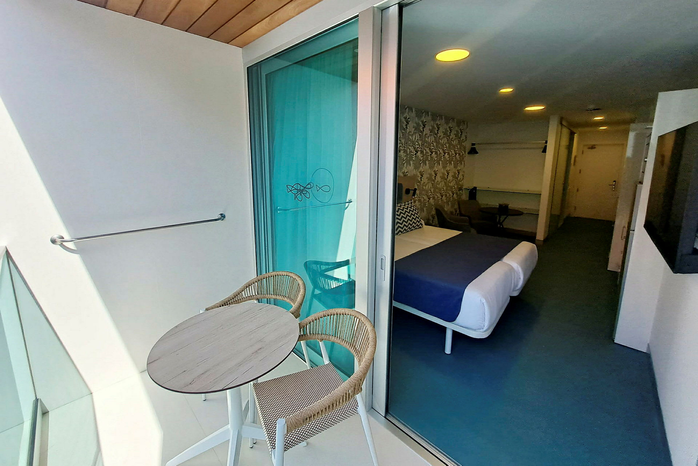 Bilde av et hotellrom med en balkong. På balkongen er det et rundt bord med to stoler. (AI-generert tekst)