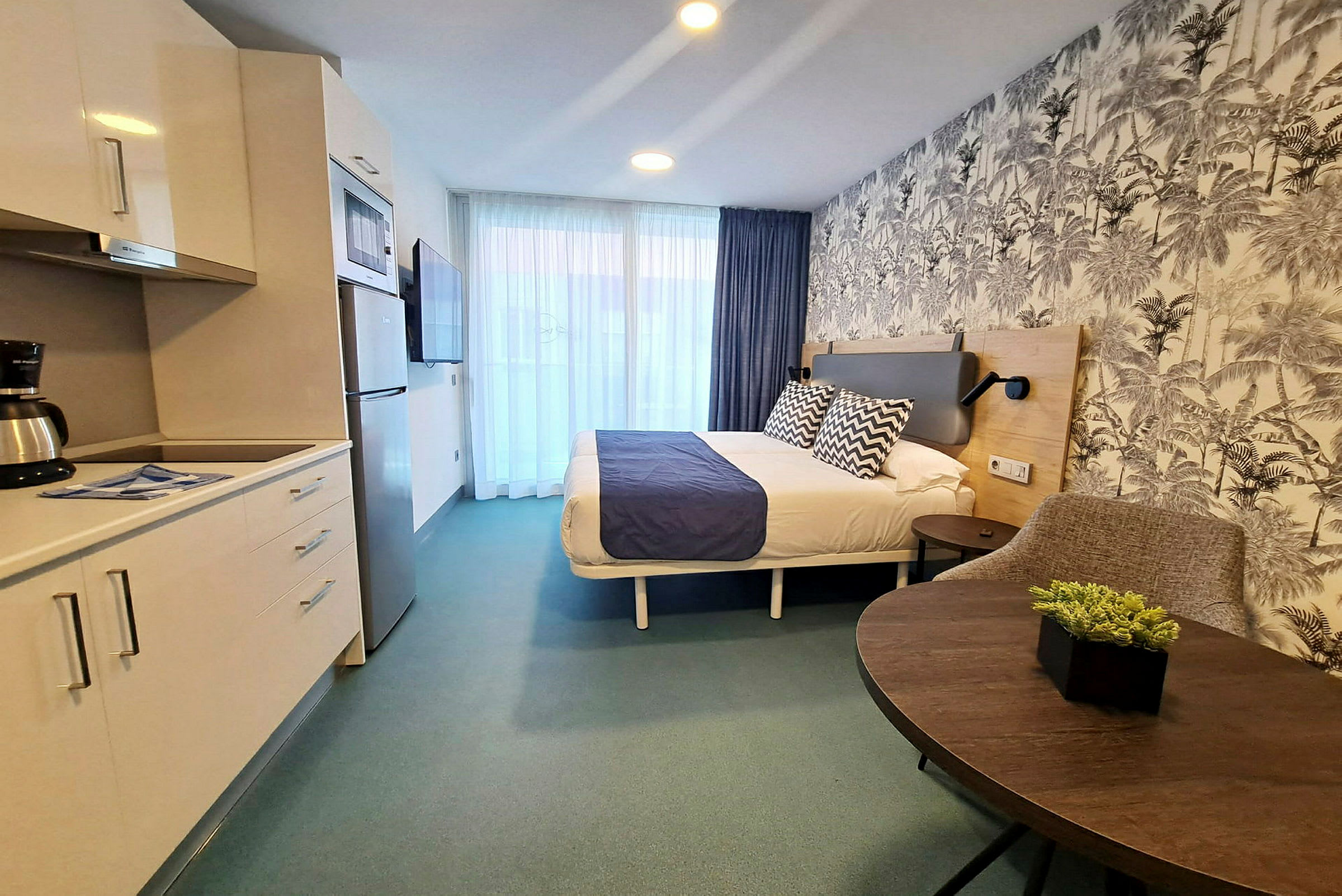 Et hotellrom med dobbeltseng, en kjøkkenkrok og en sitteplass. Veggene har mønstret tapet. (AI-generert tekst)