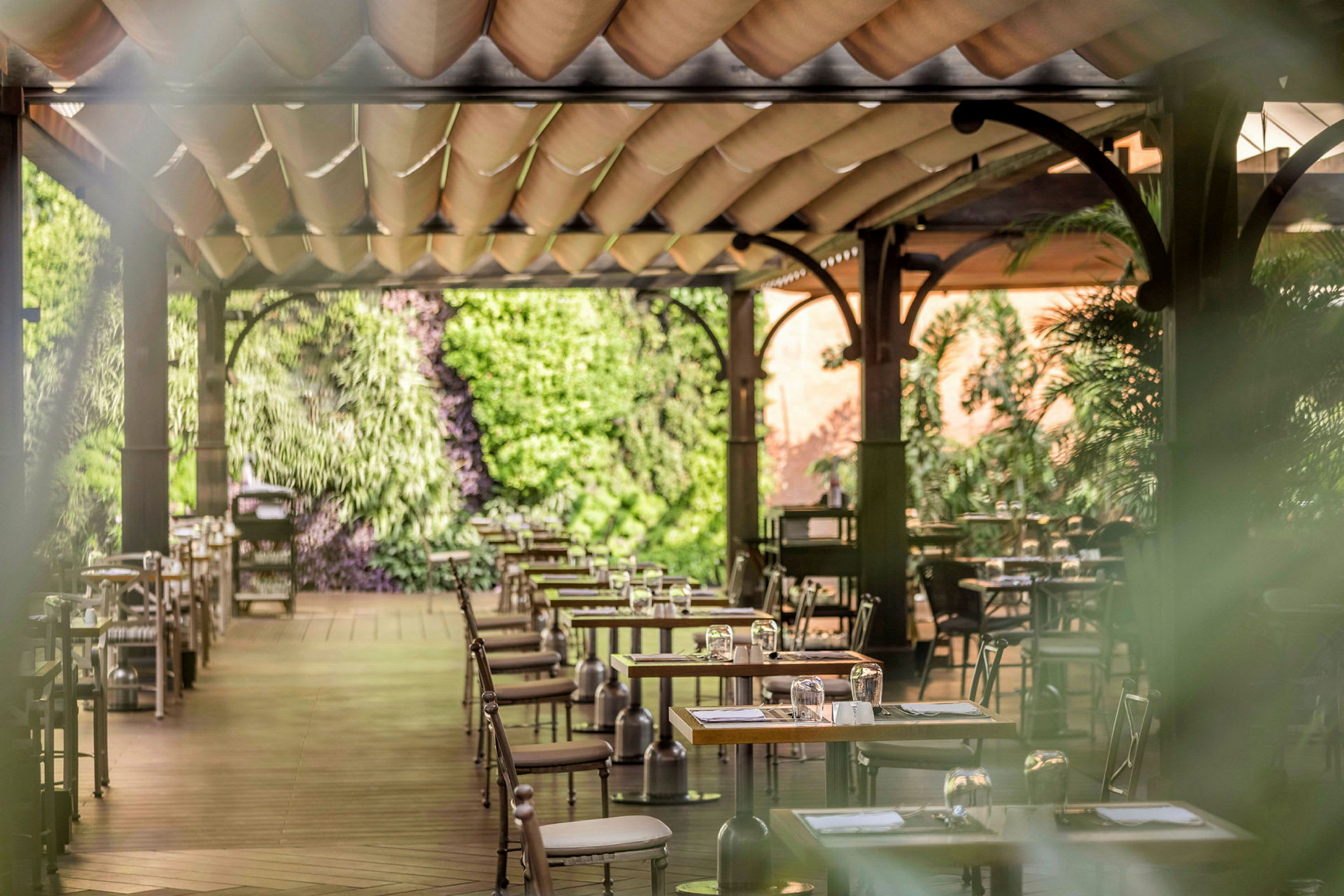 En terrasse-restaurant med trebord og stoler, dekorert med grønne planter. (AI-generert tekst)