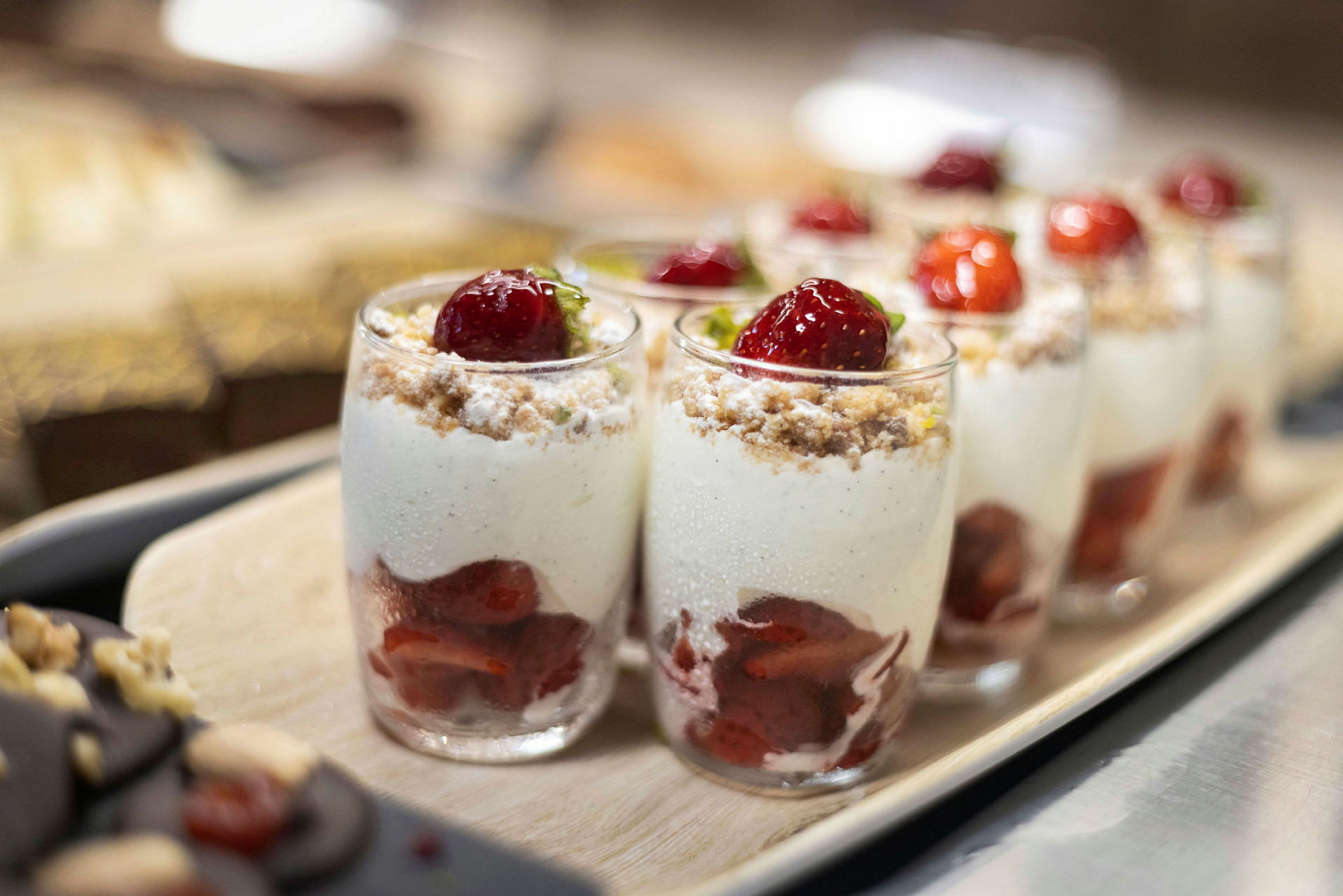 Glass med dessert bestående av jordbær, krem og smuler. (AI-generert tekst)