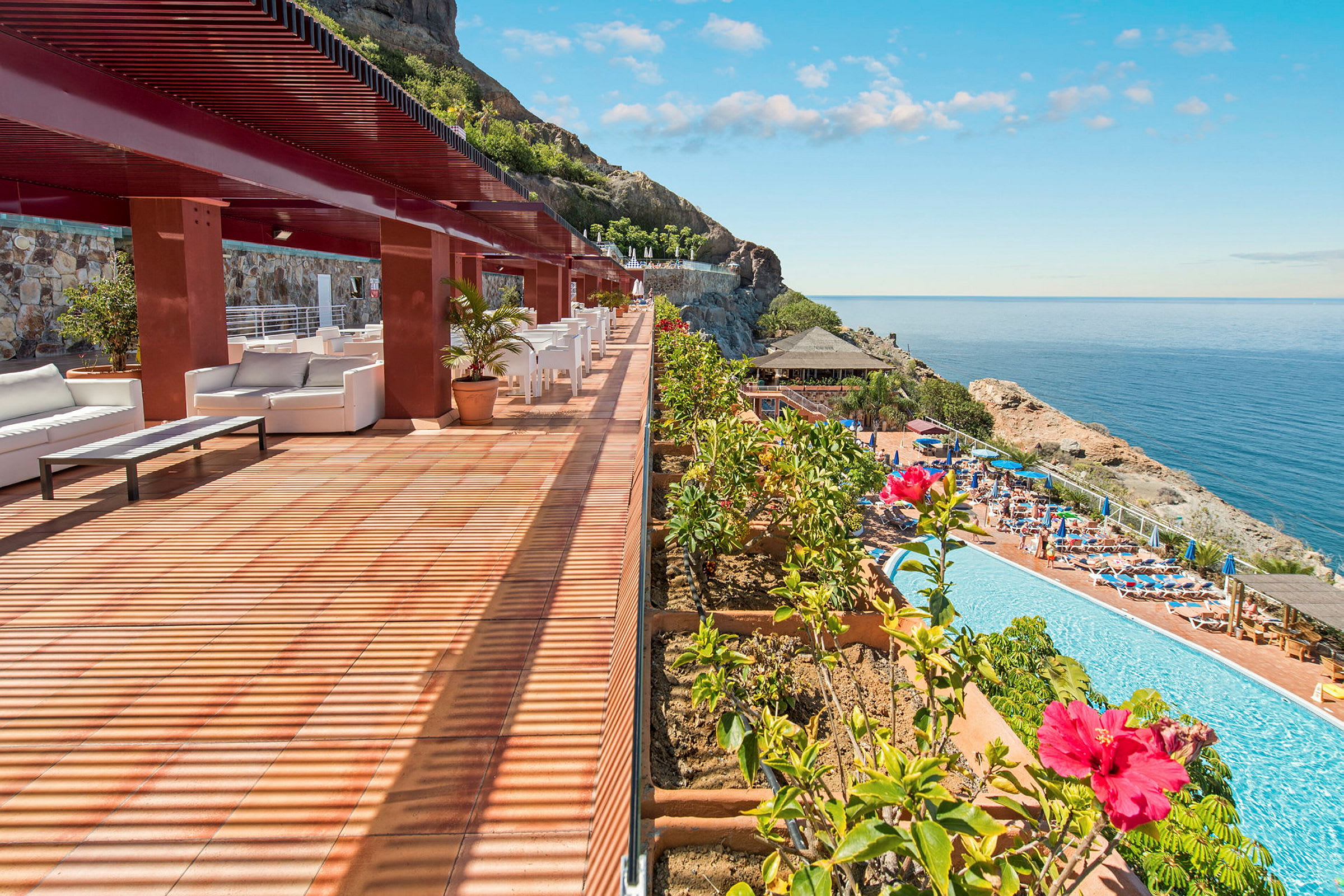 En terrasse med sitteplasser og utsikt over et basseng og havet. (AI-generert tekst)
