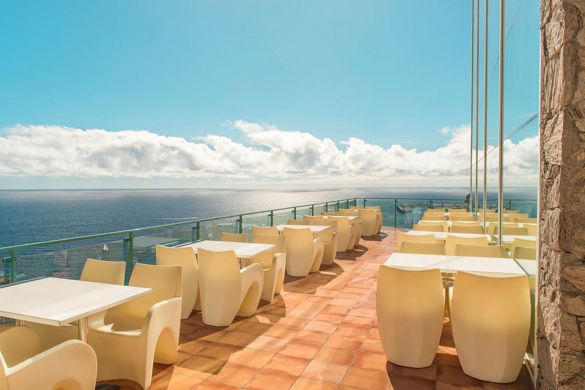 Terrasse med bord og stoler ved havet. (AI-generert tekst)