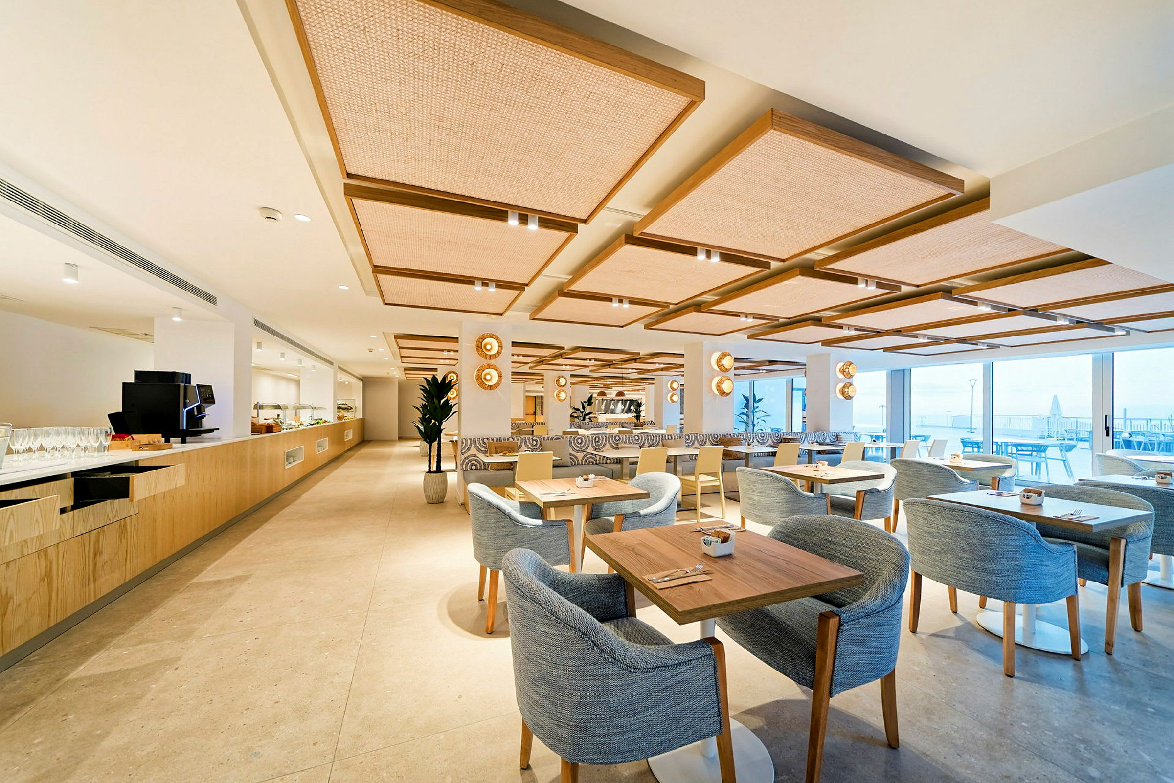 En moderne restaurant med lys innredning, bord og stoler samt store vinduer med utsikt. (AI-generert tekst)