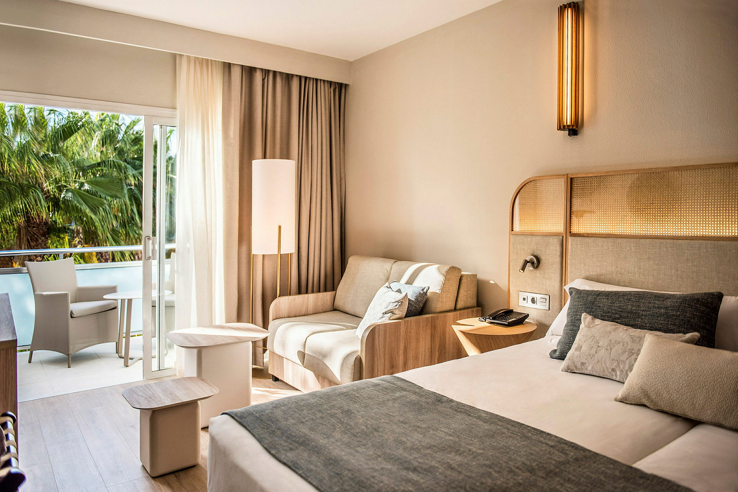 Et hotellrom med en seng, en sofa og en balkong med sittemøbler. (AI-generert tekst)