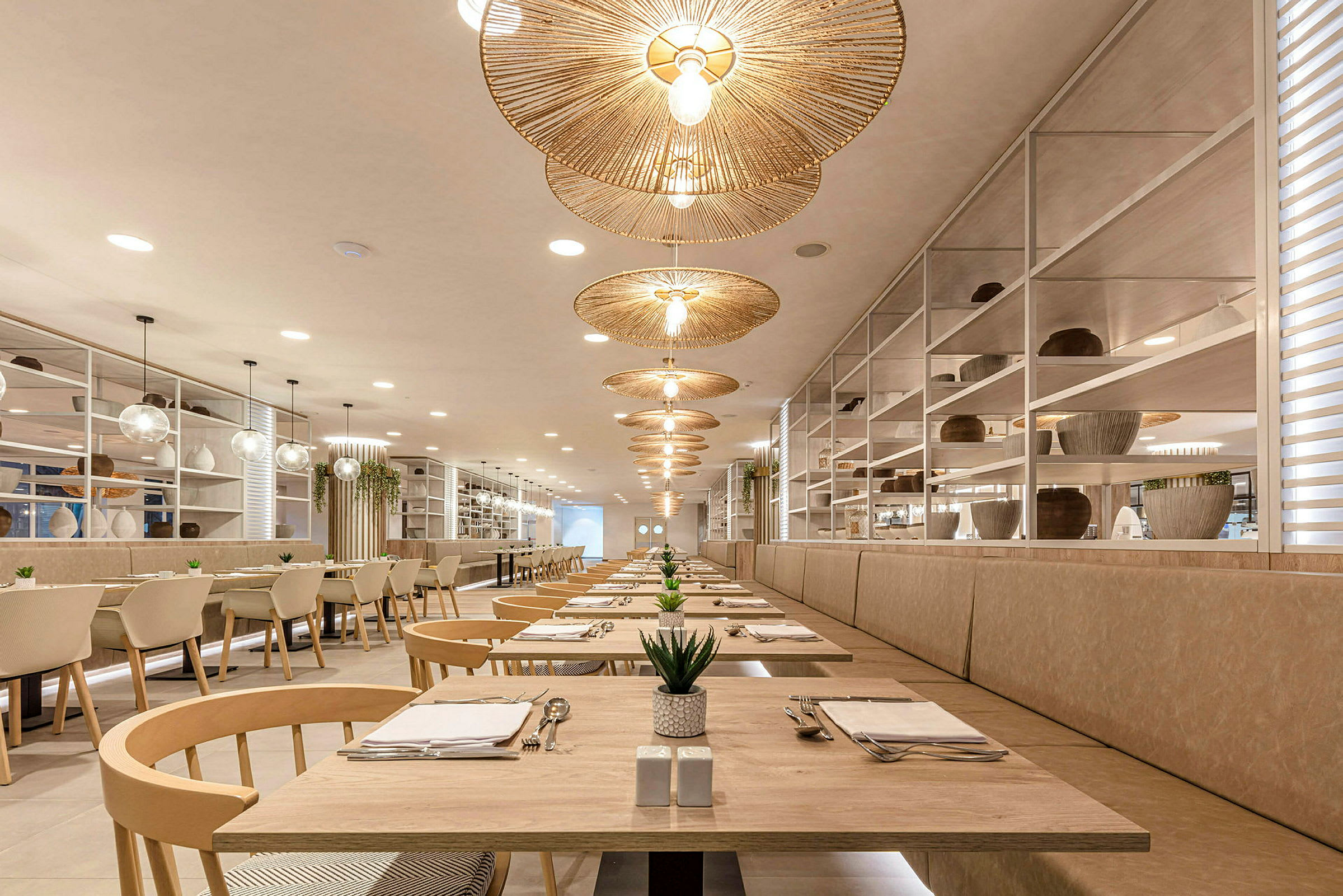 Luftig restaurant med elegante trebord, runde rottinglamper og plantepynt. (AI-generert tekst)