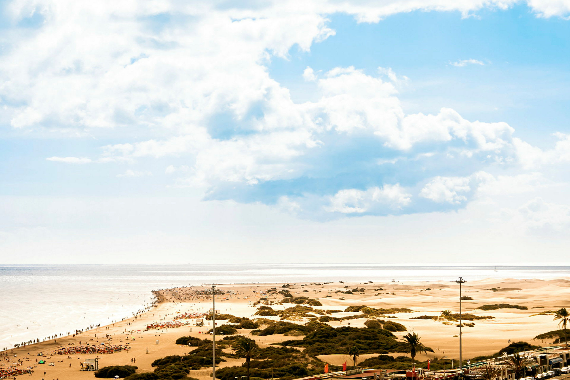 En sandstrand med mennesker og sanddyner i bakgrunnen under en blå himmel. (AI-generert tekst)