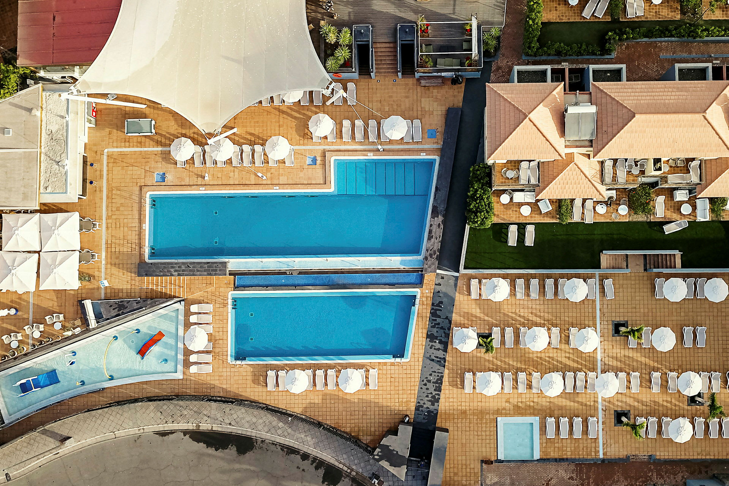Luftfoto av hotellområde med bassenger og solsenger. (AI-generert tekst)