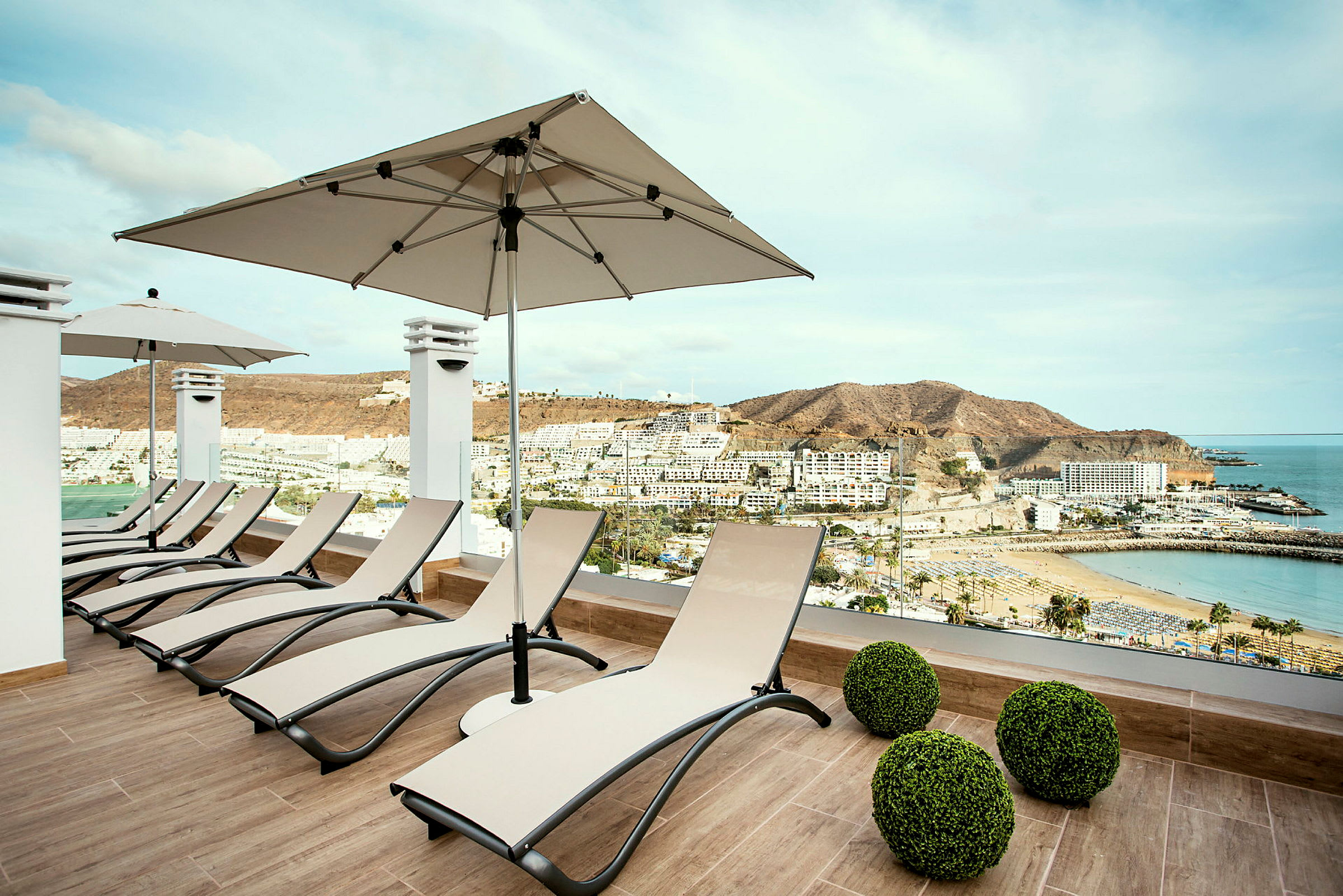 Solstoler på en terrasse med utsikt over en strand og omkringliggende bygninger. (AI-generert tekst)