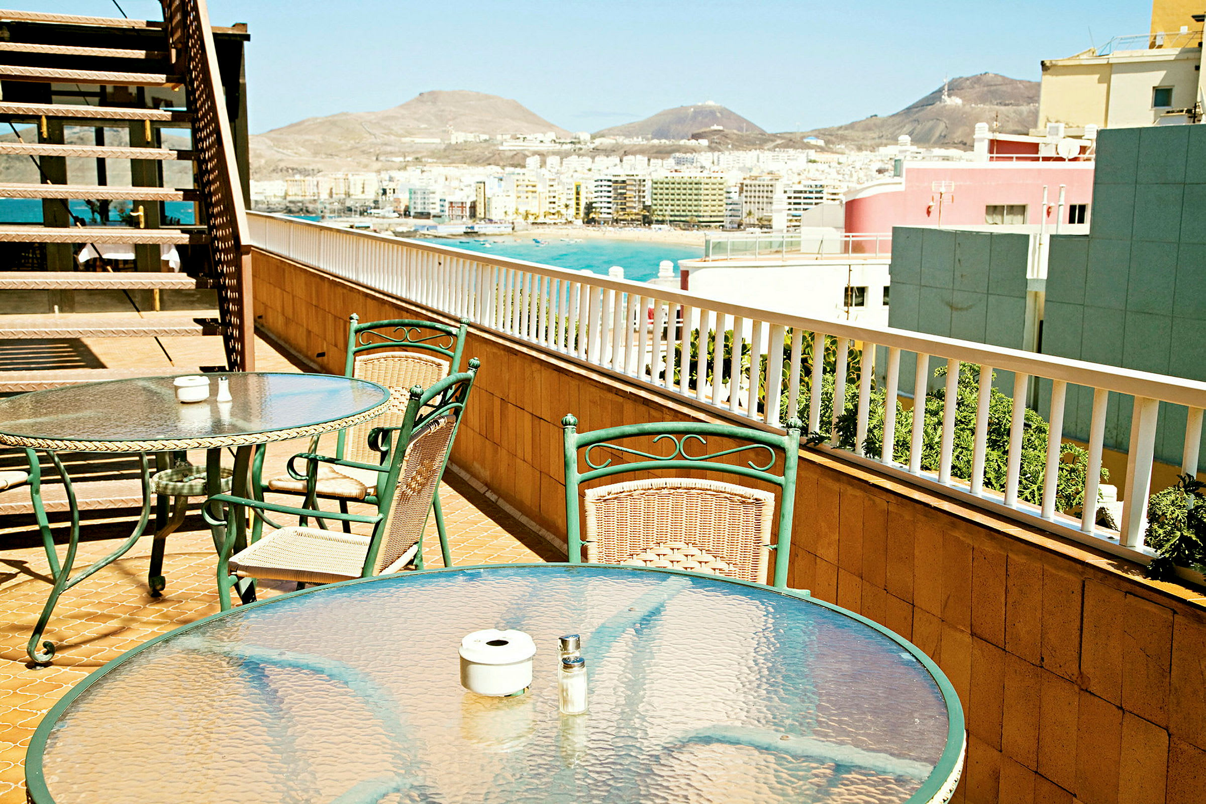 Bord og stoler på en terrasse med utsikt over en by og fjell. (AI-generert tekst)