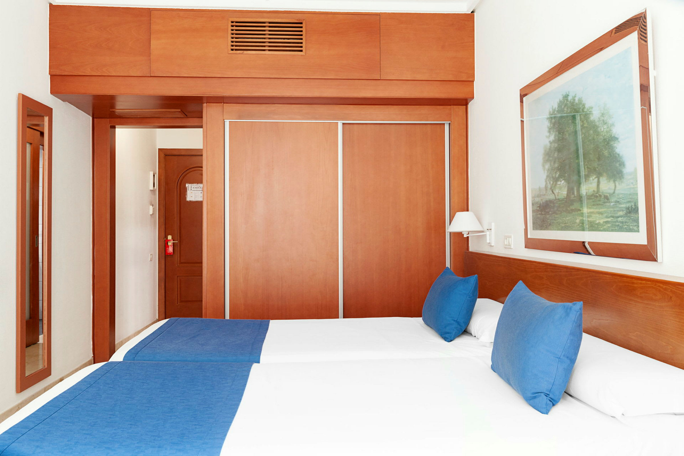 Hotellrom med to enkeltsenger, blått sengetøy og et skap med skyvedører. (AI-generert tekst)