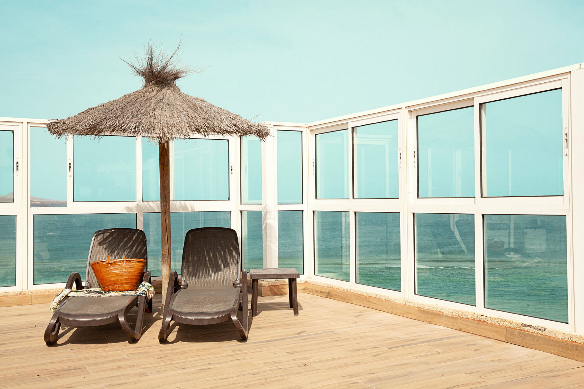 To solsenger står ved siden av en parasoll på en terrasse med utsikt over havet. (AI-generert tekst)