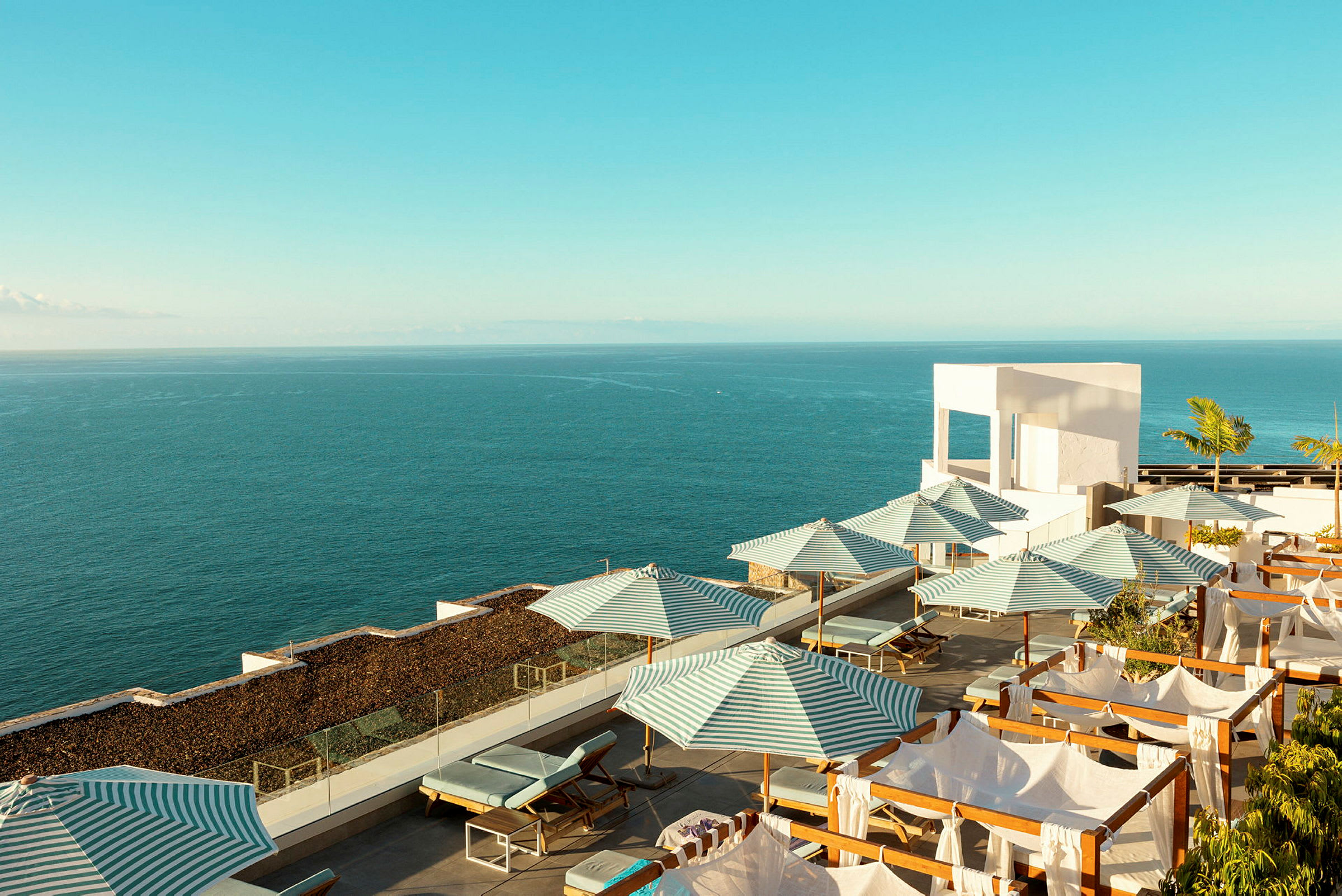 Solstoler og stripete parasoller på en terrasse ved havet. (AI-generert tekst)
