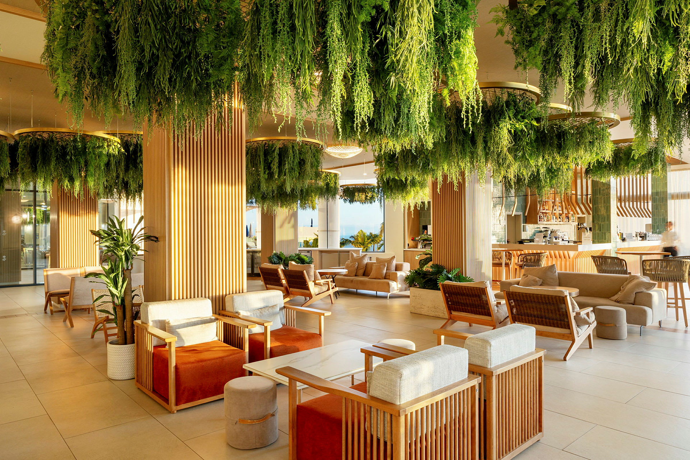 En moderne lounge med sittegrupper og grønne planter som henger fra taket. (AI-generert tekst)
