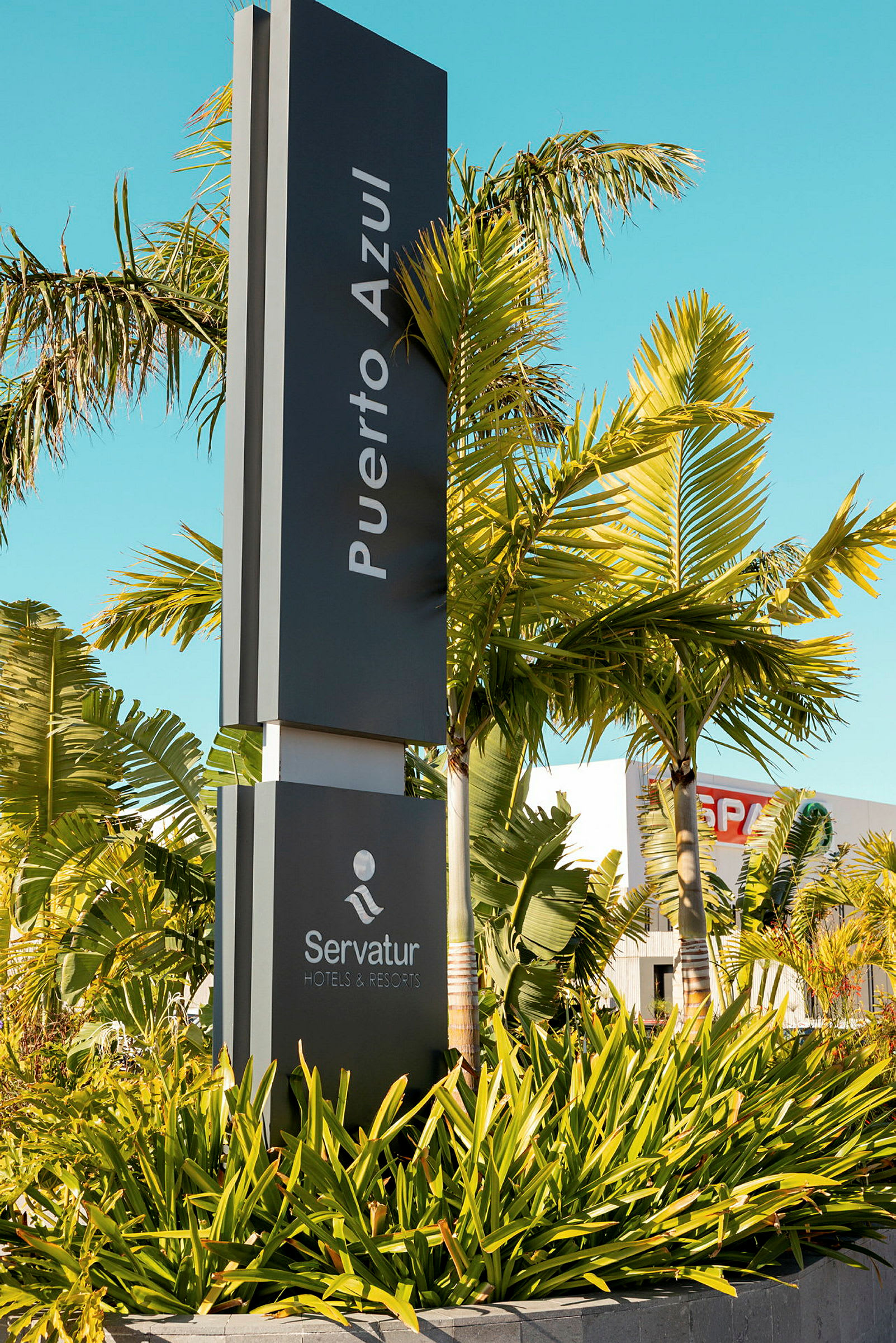 Skilt med teksten 'Puerto Azul' og 'Servatur Hotels & Resorts', omgitt av palmer og grøntområder. (AI-generert tekst)