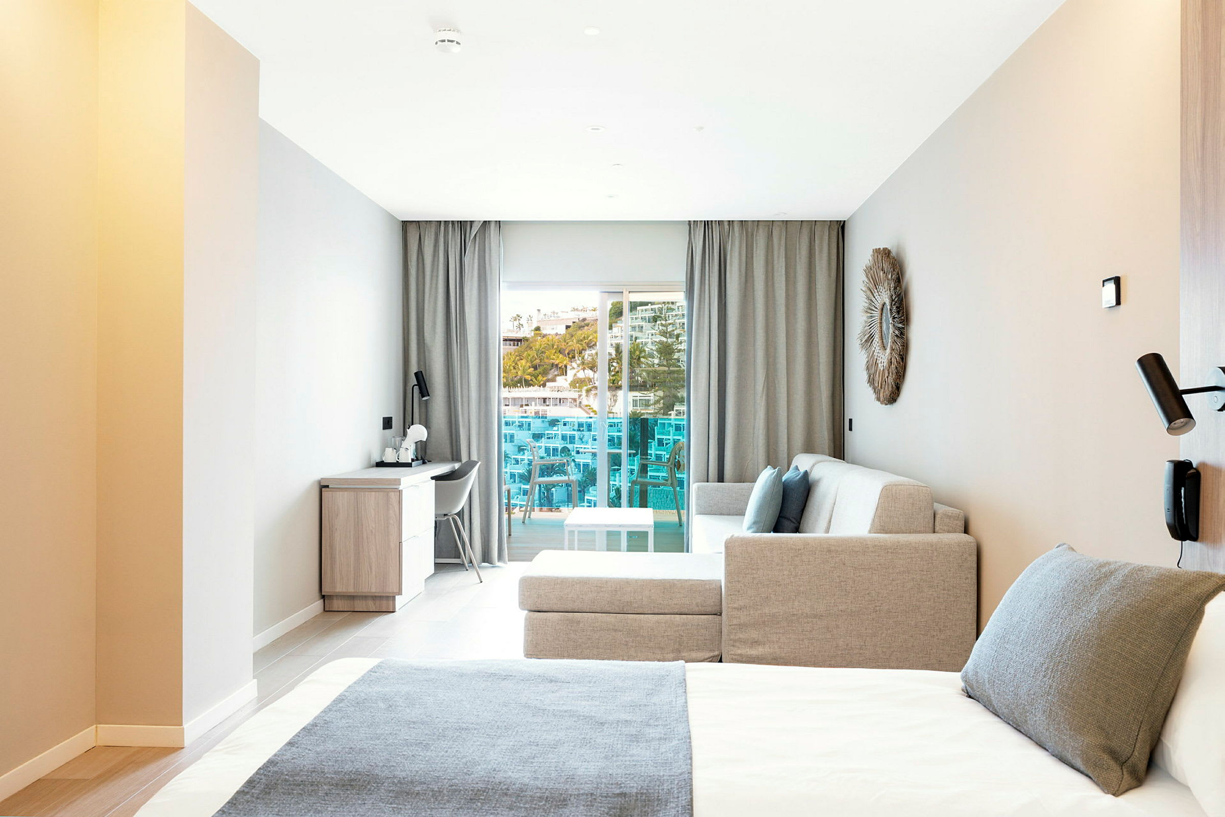 Moderne hotellrom med seng, sofa og skrivebord, samt en balkong med utsikt. (AI-generert tekst)