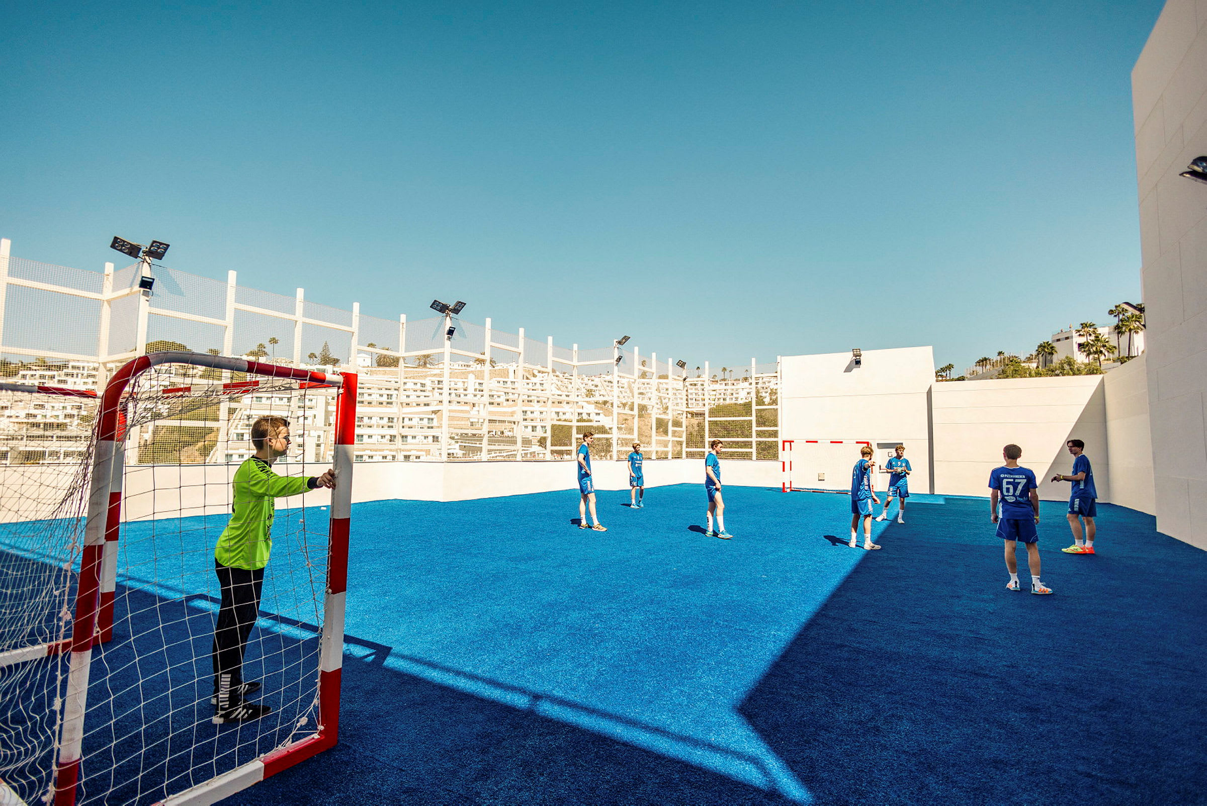 Flere personer spiller fotball på en utendørsbane med blått underlag. (AI-generert tekst)