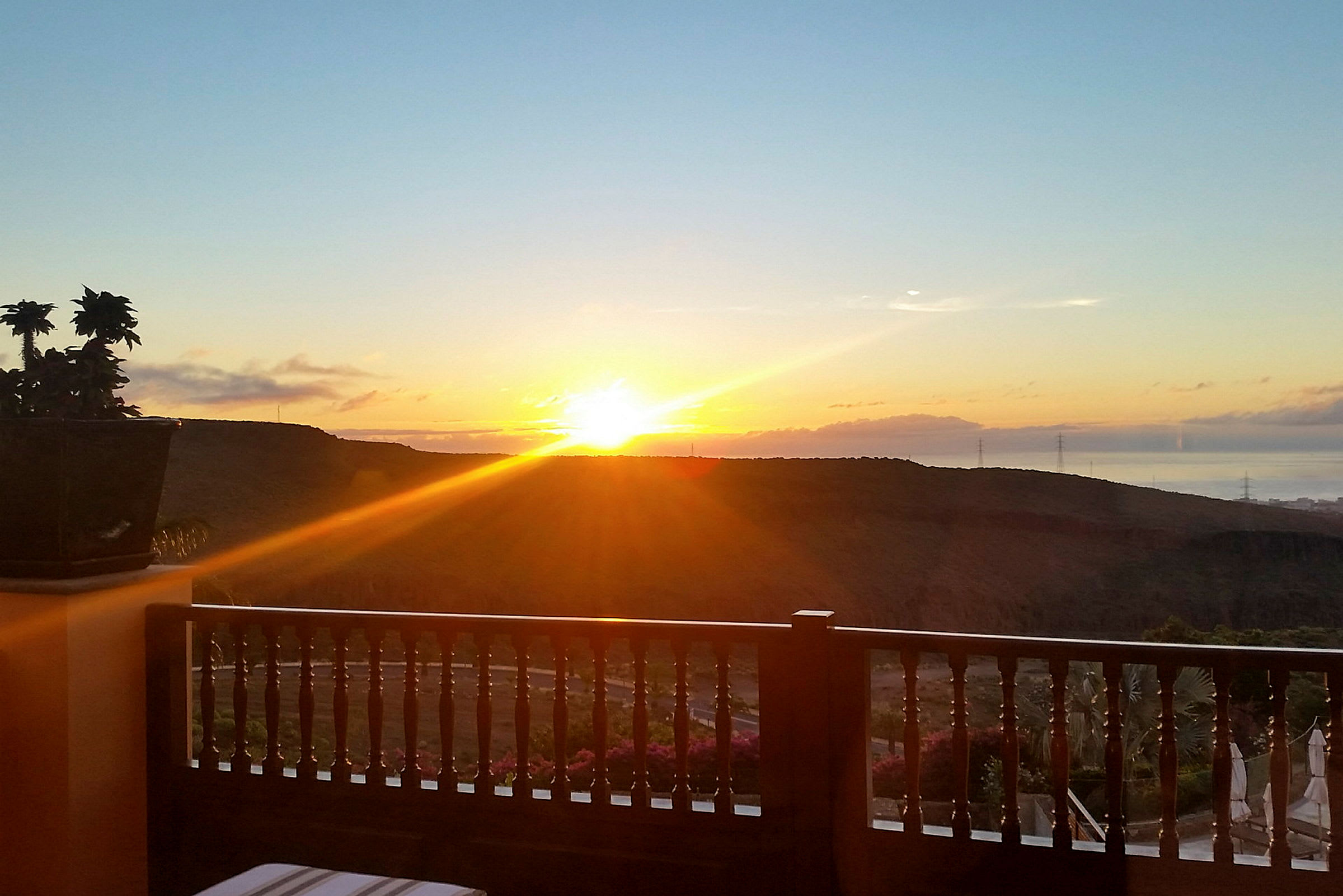 Solnedgang over et landskap med åser, sett fra en balkong med tre rekkverk. (AI-generert tekst)