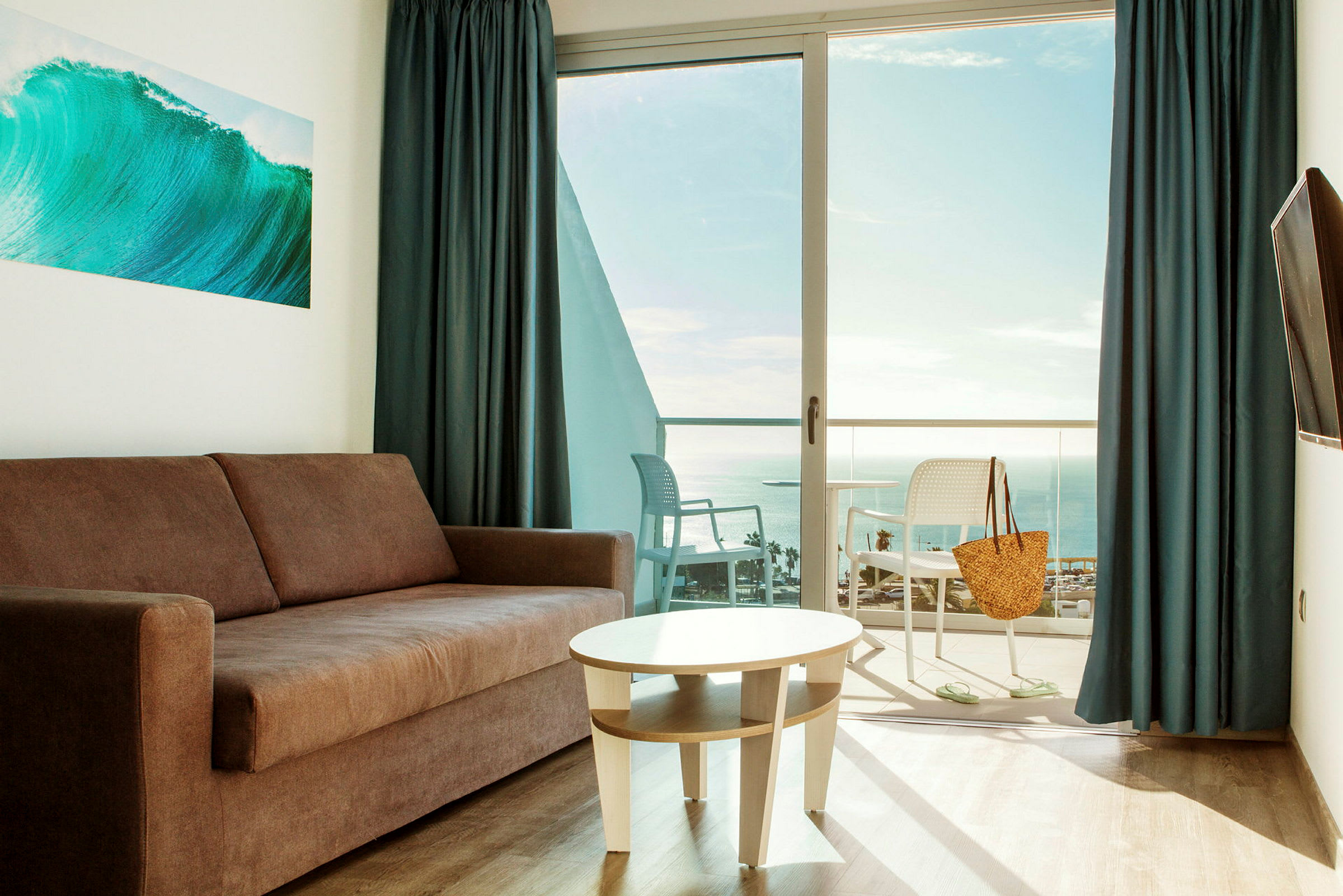 En stue med sofa og bord, med en balkong og utsikt over havet. (AI-generert tekst)