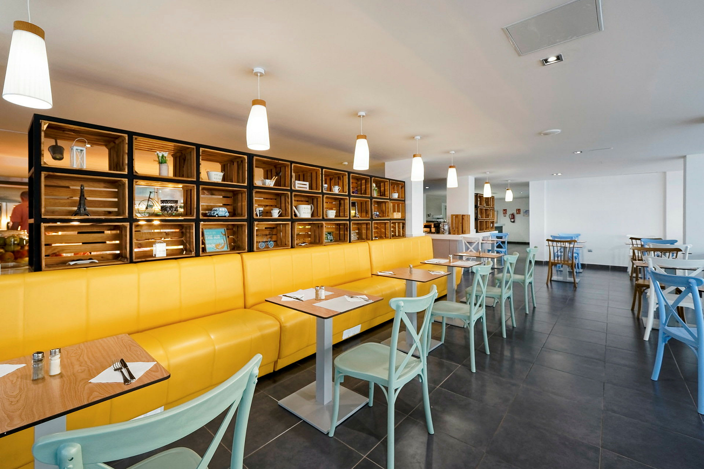 Restaurant med gul sofa, lyse stoler og dekorativ trebokhylle. (AI-generert tekst)