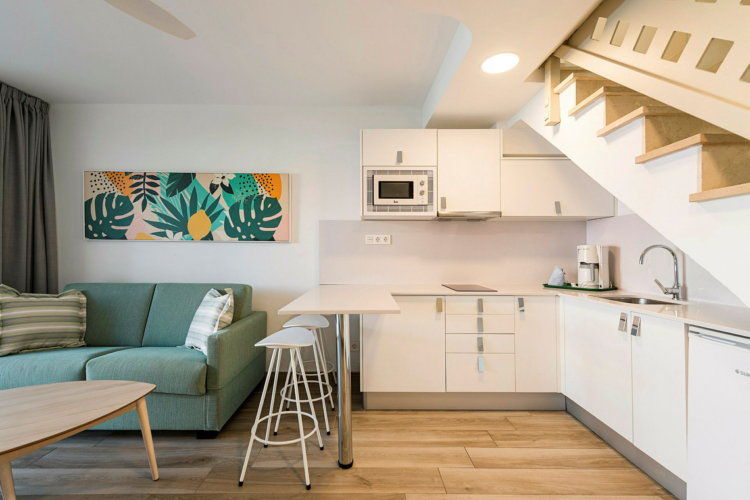 Moderne stue med grønn sofa og fullt utstyrt kjøkken samt trapp opp til overetasjen. (AI-generert tekst)