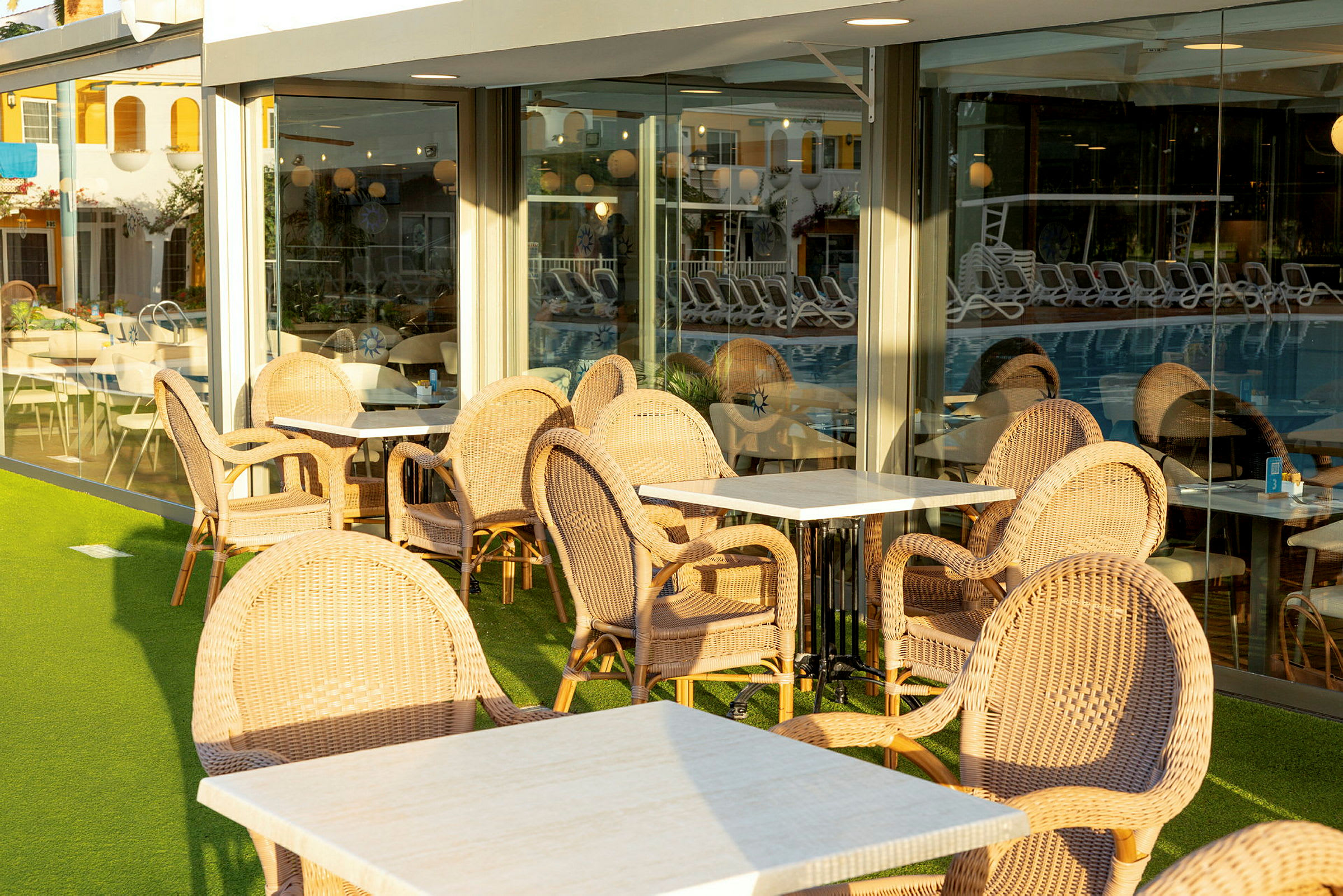 Utemøbler på en kafé eller restaurant, med flettede stoler og bord, plassert ved store vinduer. (AI-generert tekst)