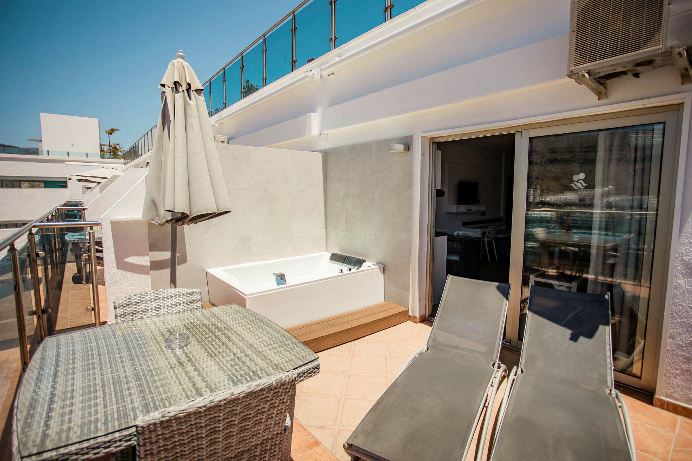 Privat terrasse med bord, stoler, solsenger og et boblebad. (AI-generert tekst)