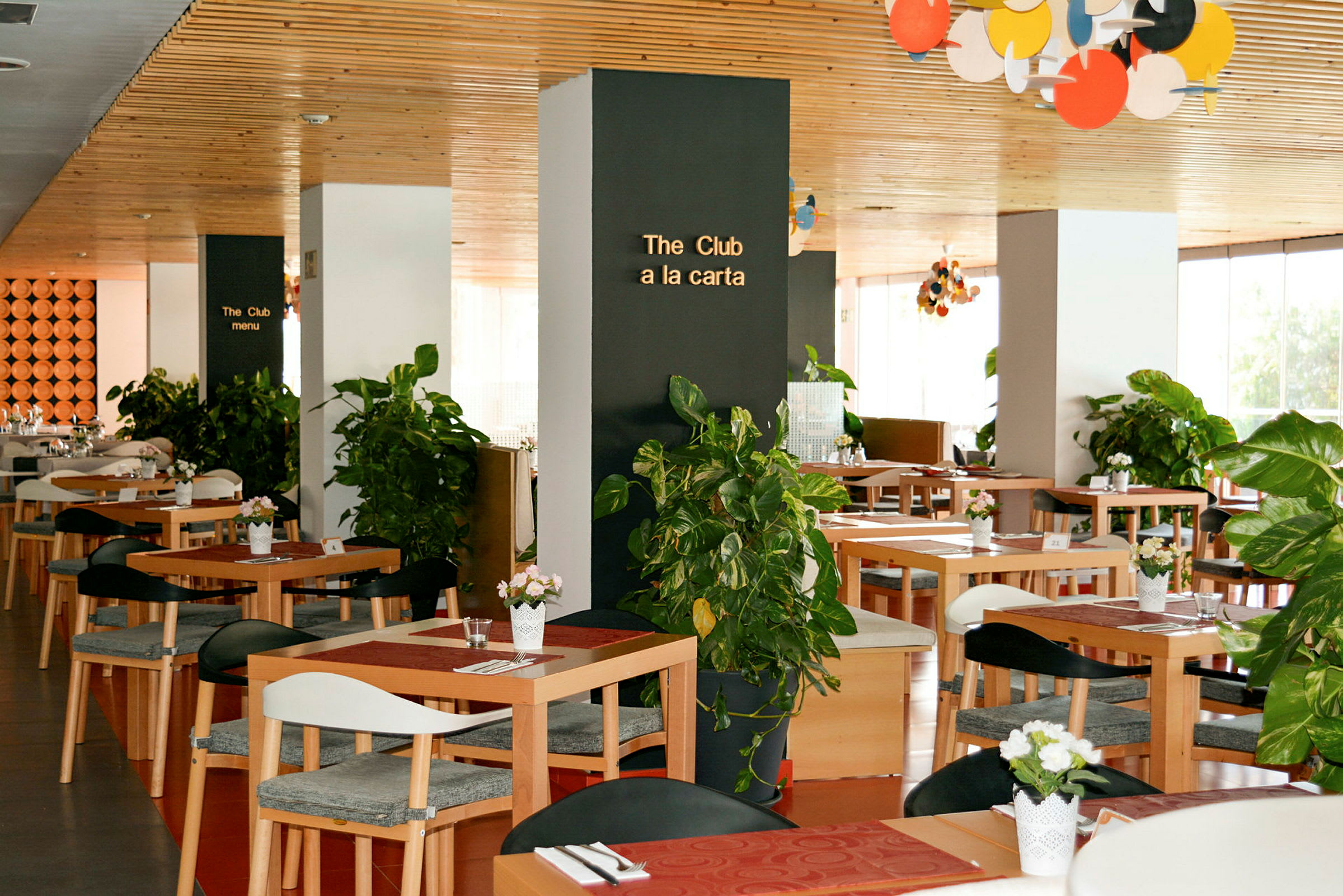 En restaurant med trebord og dekorasjoner av grønne planter. (AI-generert tekst)