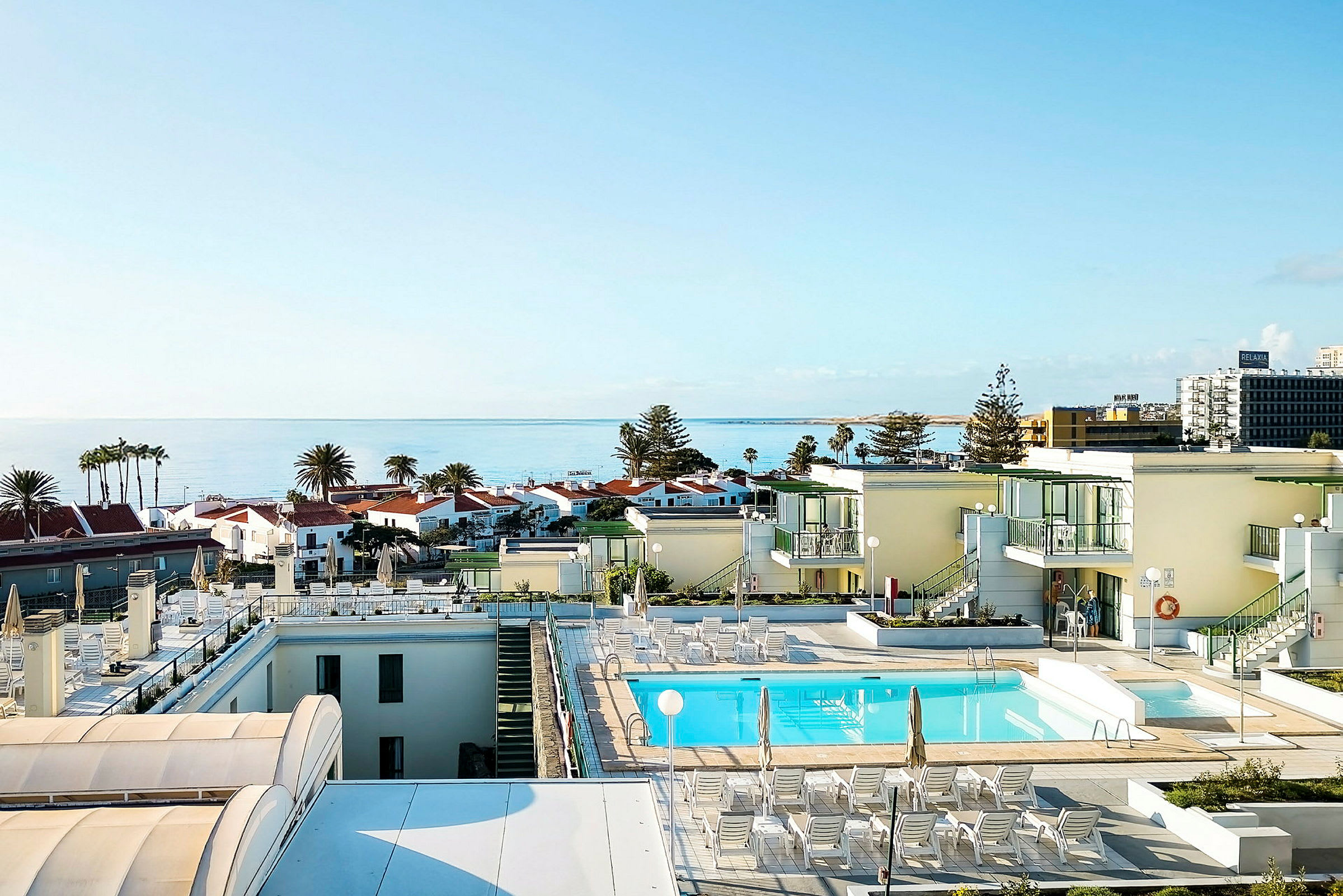 Utsikt over et basseng på et hotell med havet og bygninger i bakgrunnen. (AI-generert tekst)