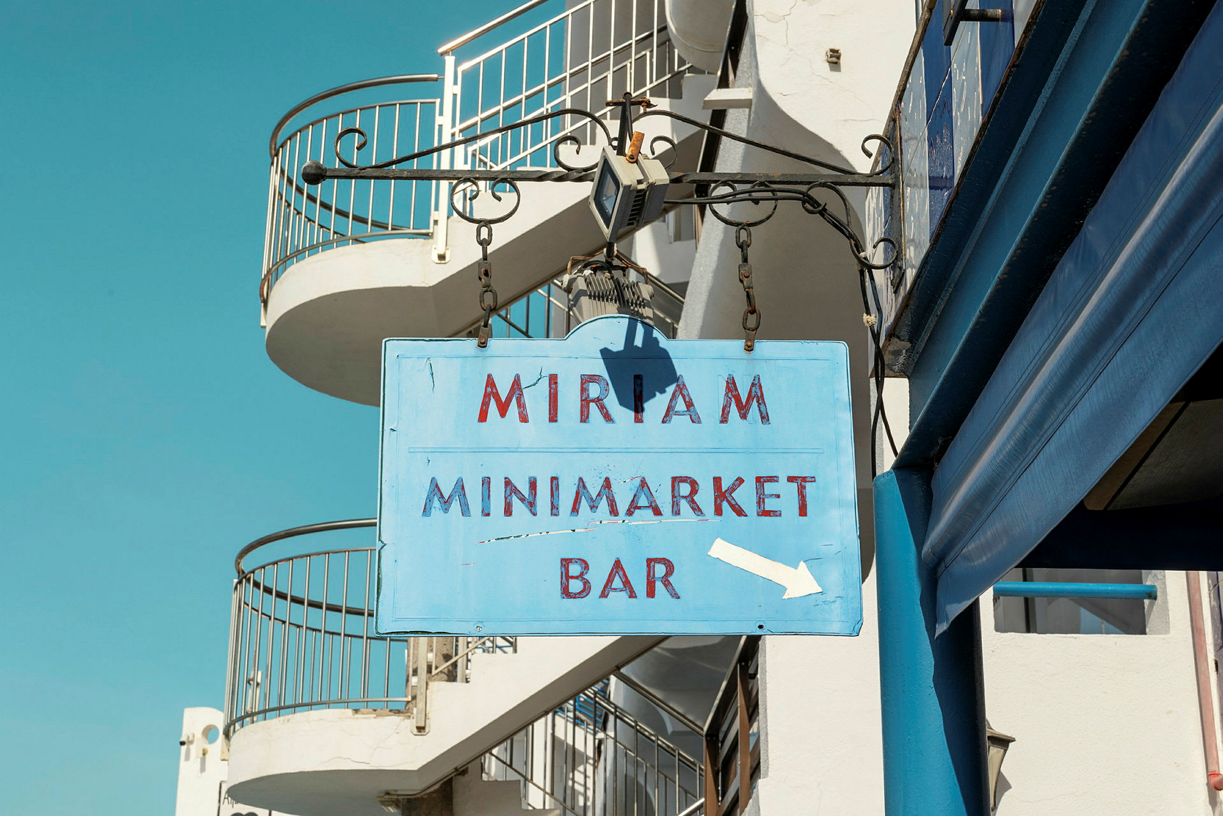 Skilt med teksten 'Miriam Minimarket Bar' som henger på en bygning. (AI-generert tekst)