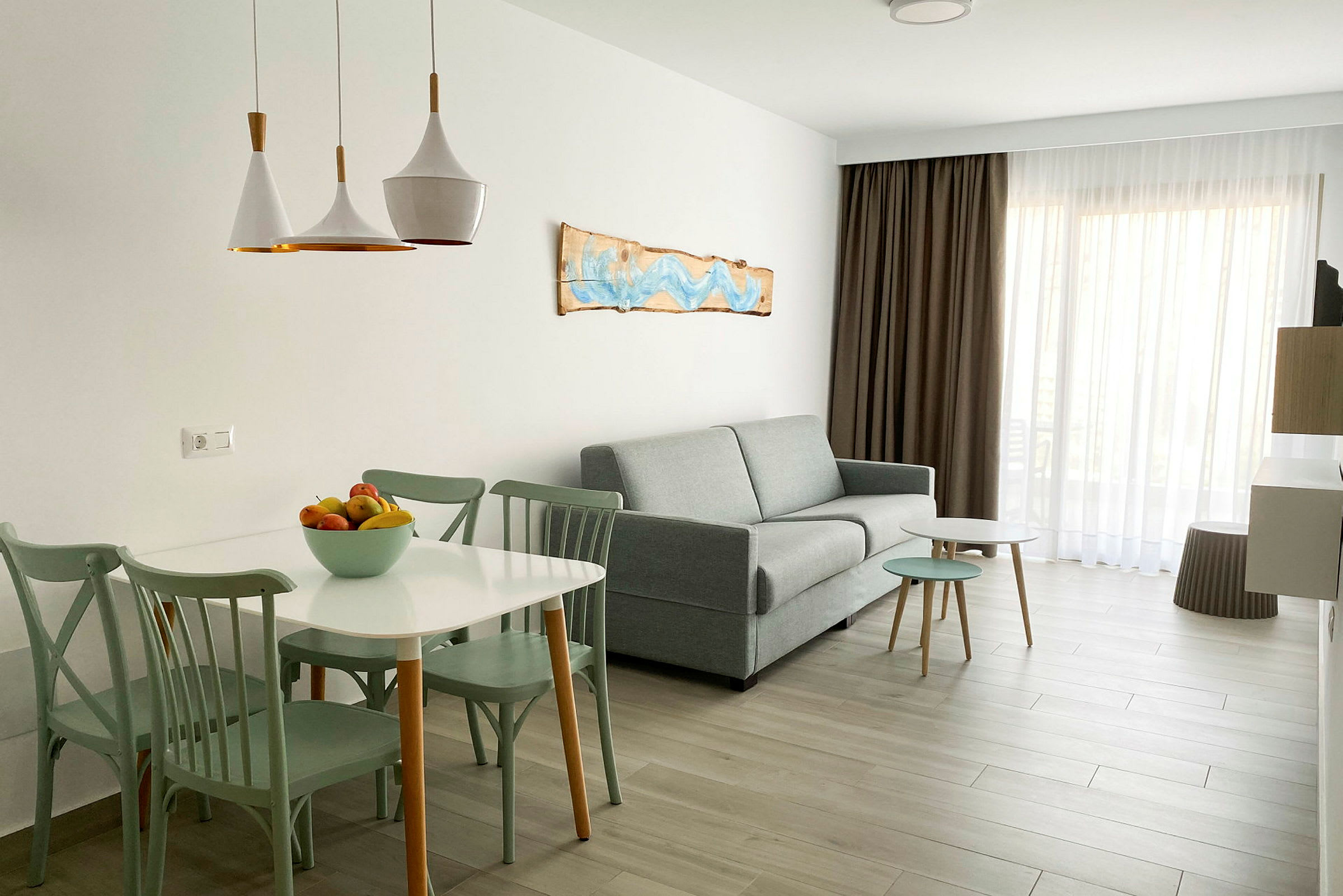 En lys og moderne stueinteriør med sofa, bord og stoler, samt en bolle med frukt på bordet. (AI-generert tekst)