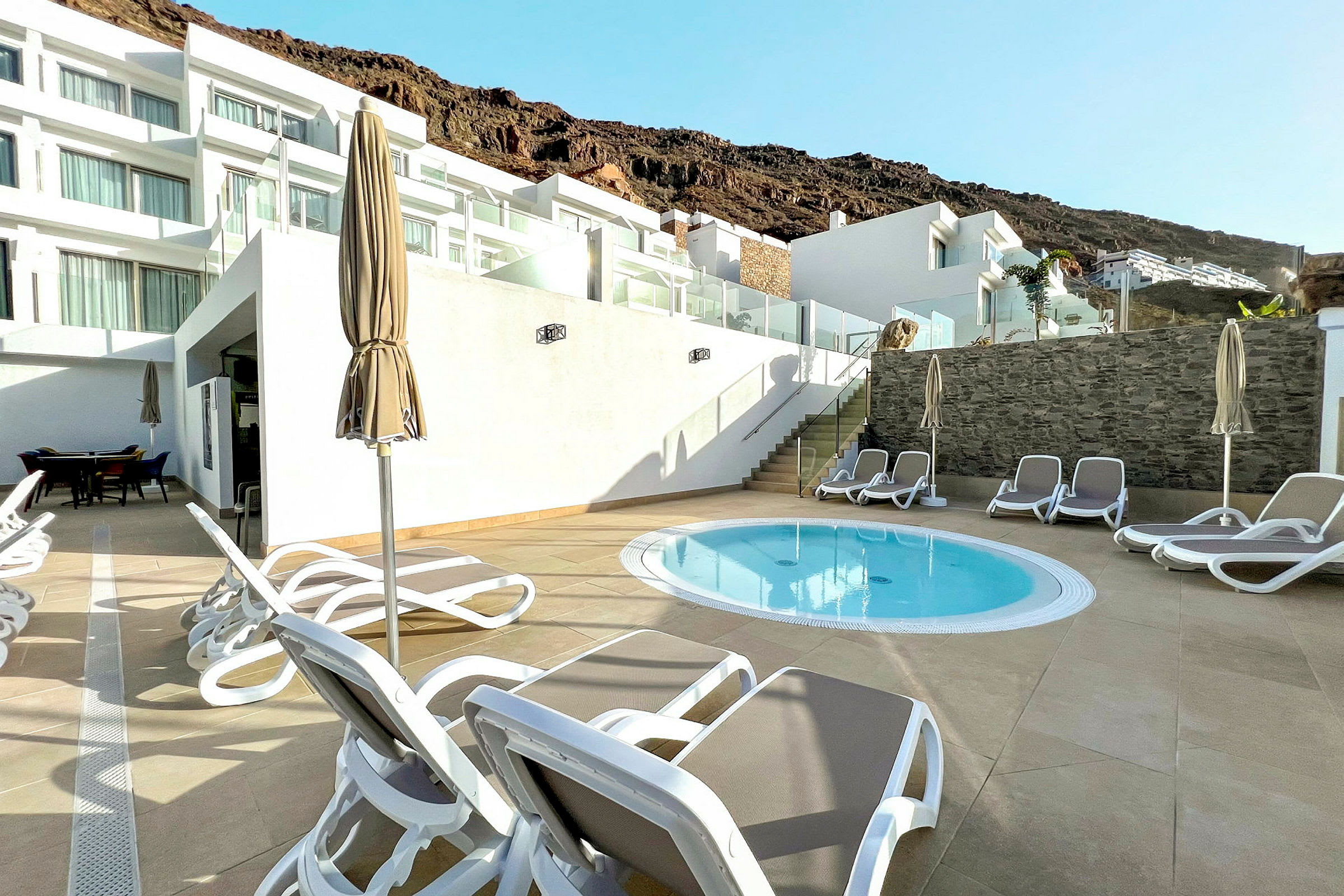 Liten basseng med solsenger og parasoller på en terrasse ved et hotell. (AI-generert tekst)