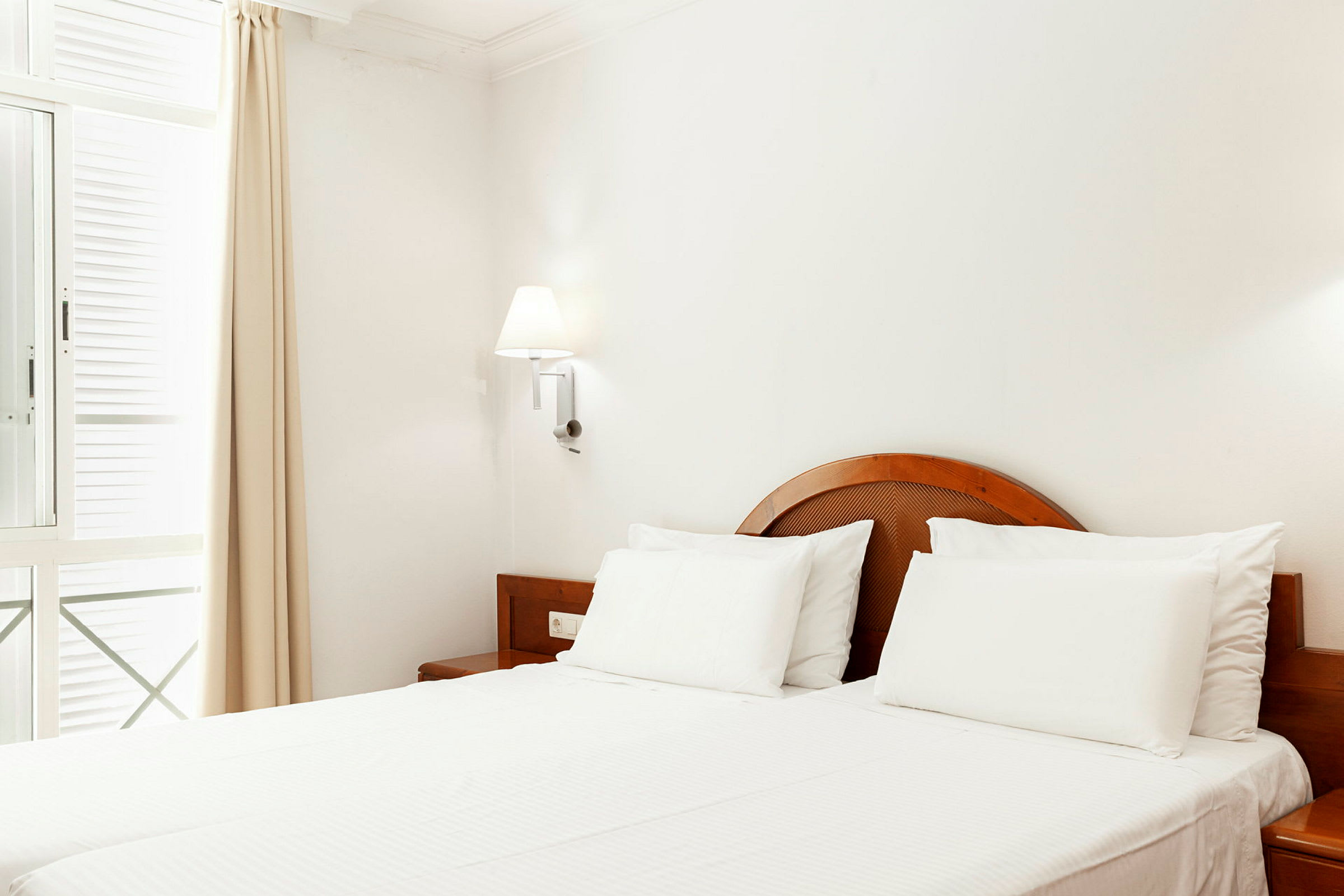 Lyst hotellrom med en dobbeltseng og tremøbler. (AI-generert tekst)
