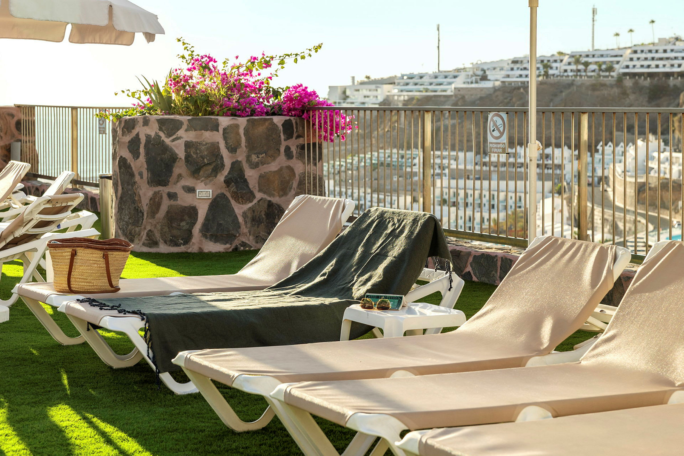 Solstoler på en terrasse med utsikt over en by og blomster i en steinkrukke benyttes. (AI-generert tekst)