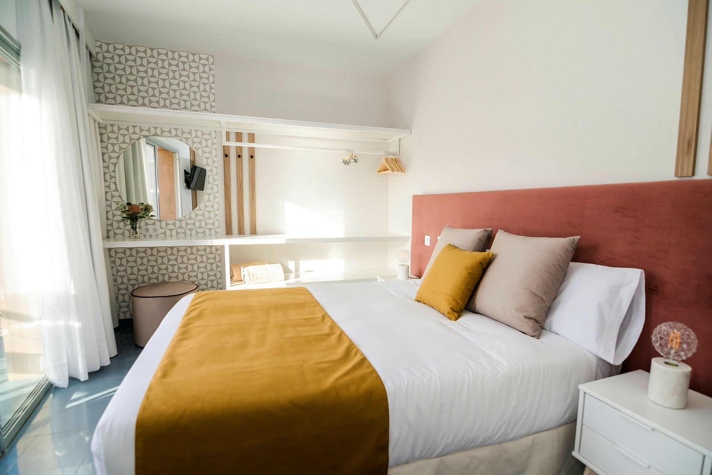 Et hotellrom med en dobbeltseng, gul sengeteppe og rosa sengegavel, samt en moderne innredning med hyller, speil og lys dekorasjon. (AI-generert tekst)