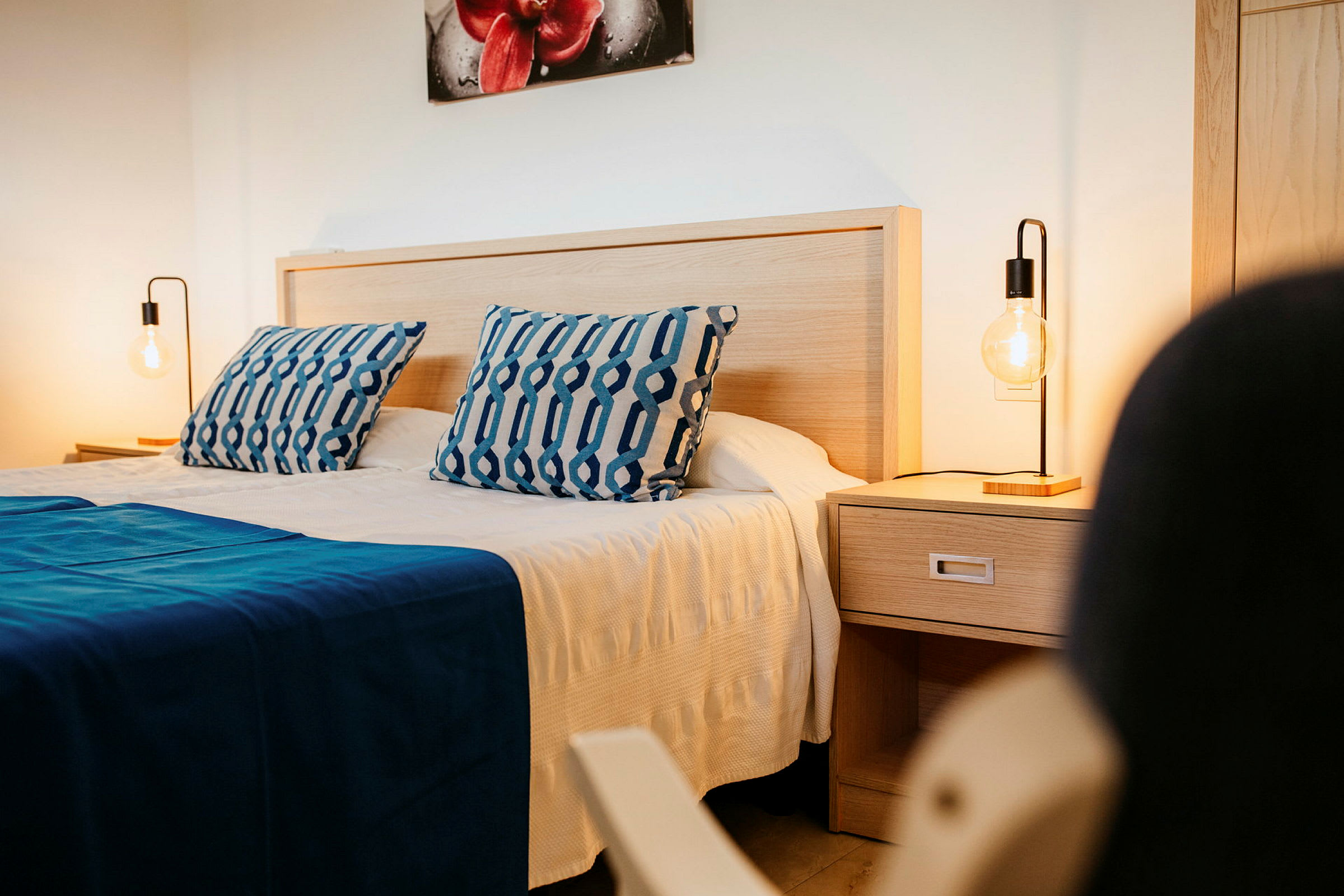 Tomannsrom med blå puter og sengeteppe, nattbord med en lampe. (AI-generert tekst)