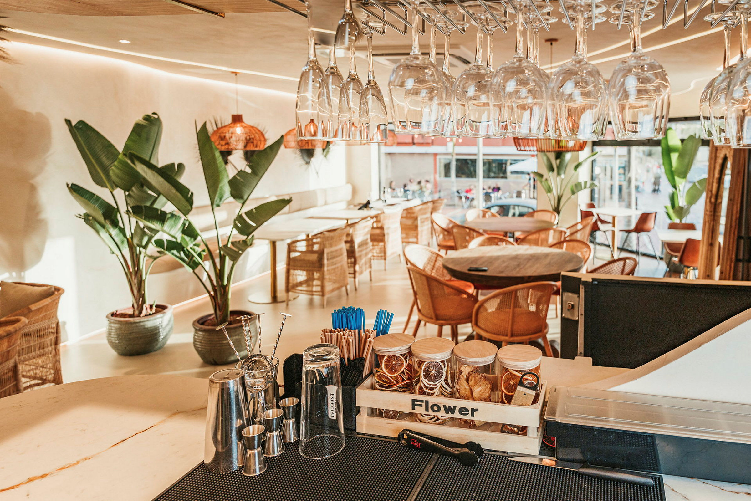 En moderne kafé med glass, store grønne planter og stoler i flettverk. (AI-generert tekst)