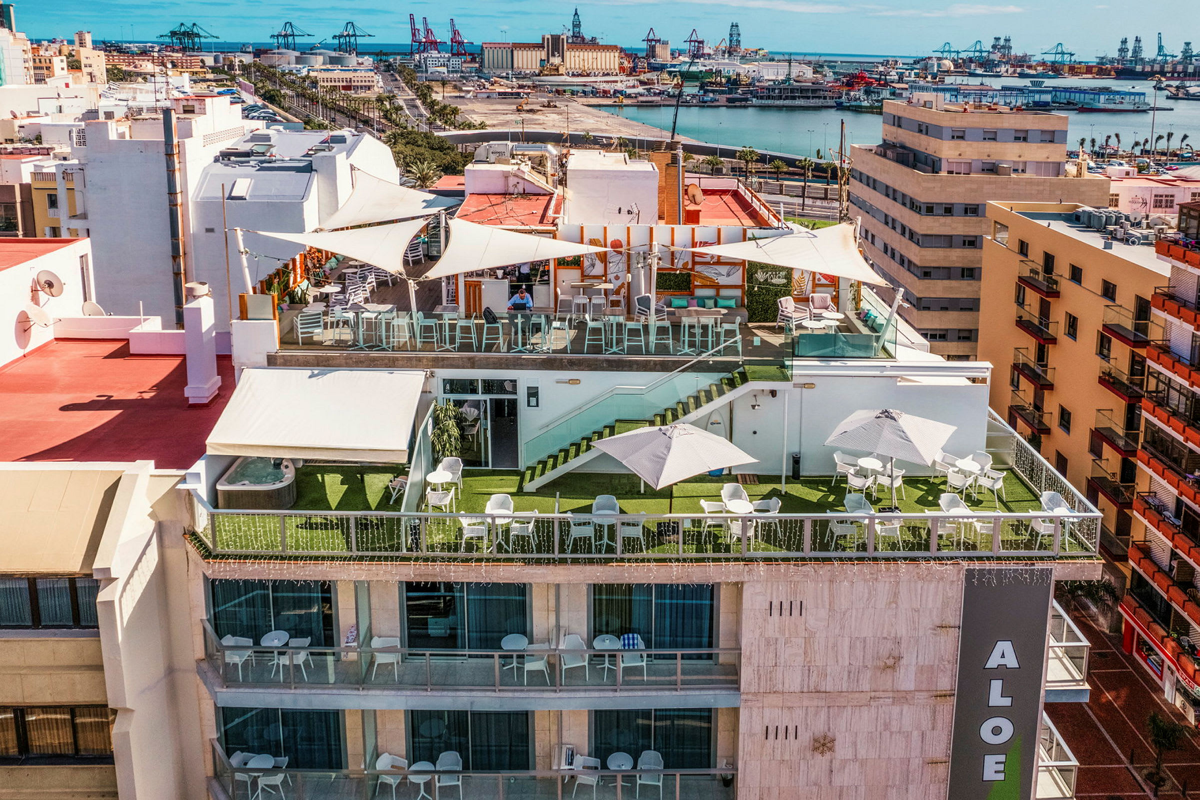 Hotellterrasse med sittegrupper, parasoller og utsikt over byen og havnen. (AI-generert tekst)