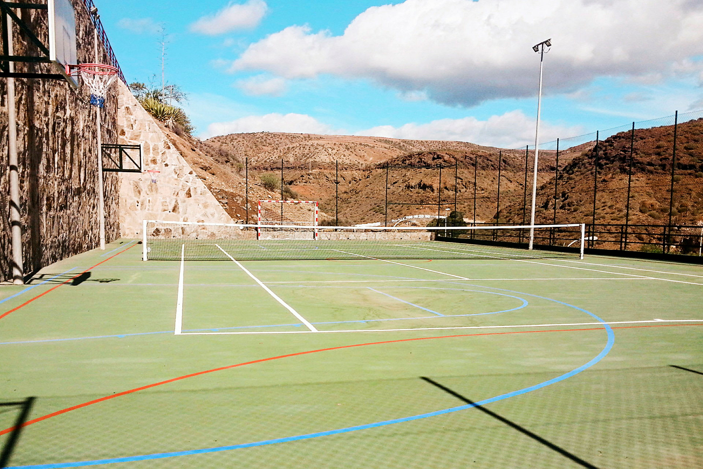 Bilde av en utendørs idrettsplass med nett for tennis, fotballmål og basketballkurv. (AI-generert tekst)