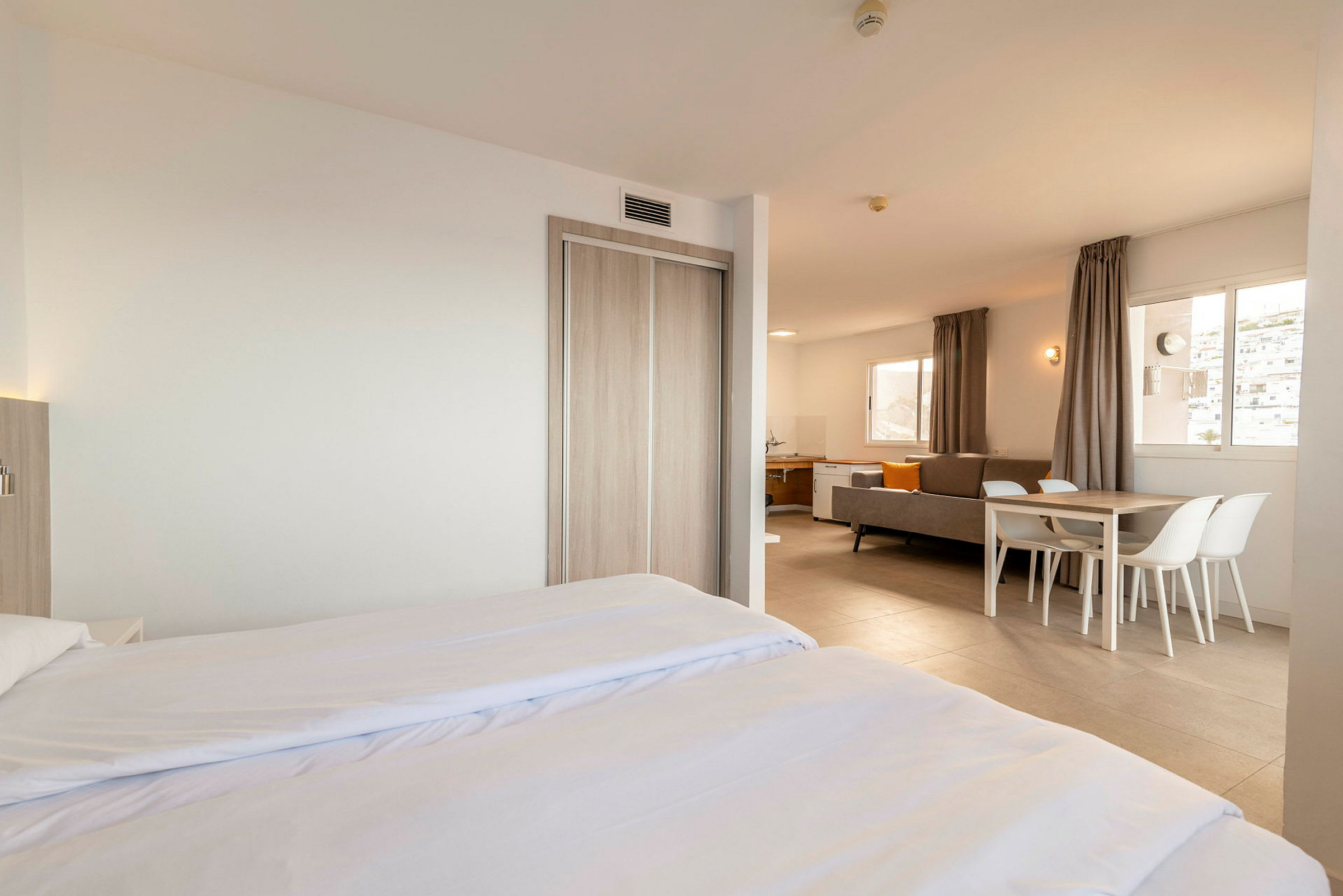 Moderne og lyst innredet hotellrom med dobbeltseng, sittegruppe og spisebord. (AI-generert tekst)