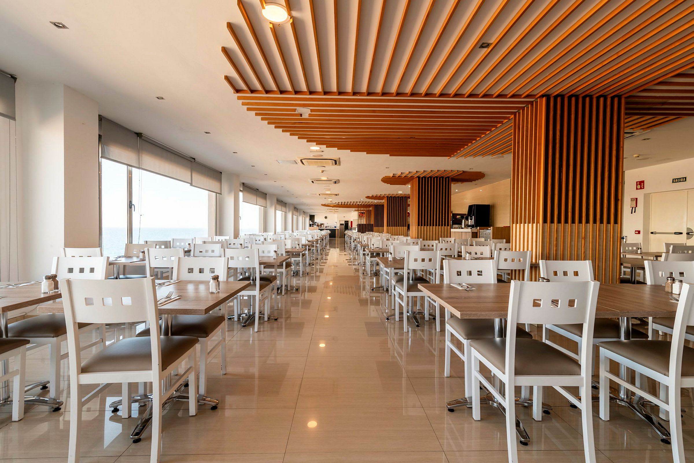 Bilde av en romslig og lys restaurant med hvite bord og stoler, samt treelementer i taket. (AI-generert tekst)