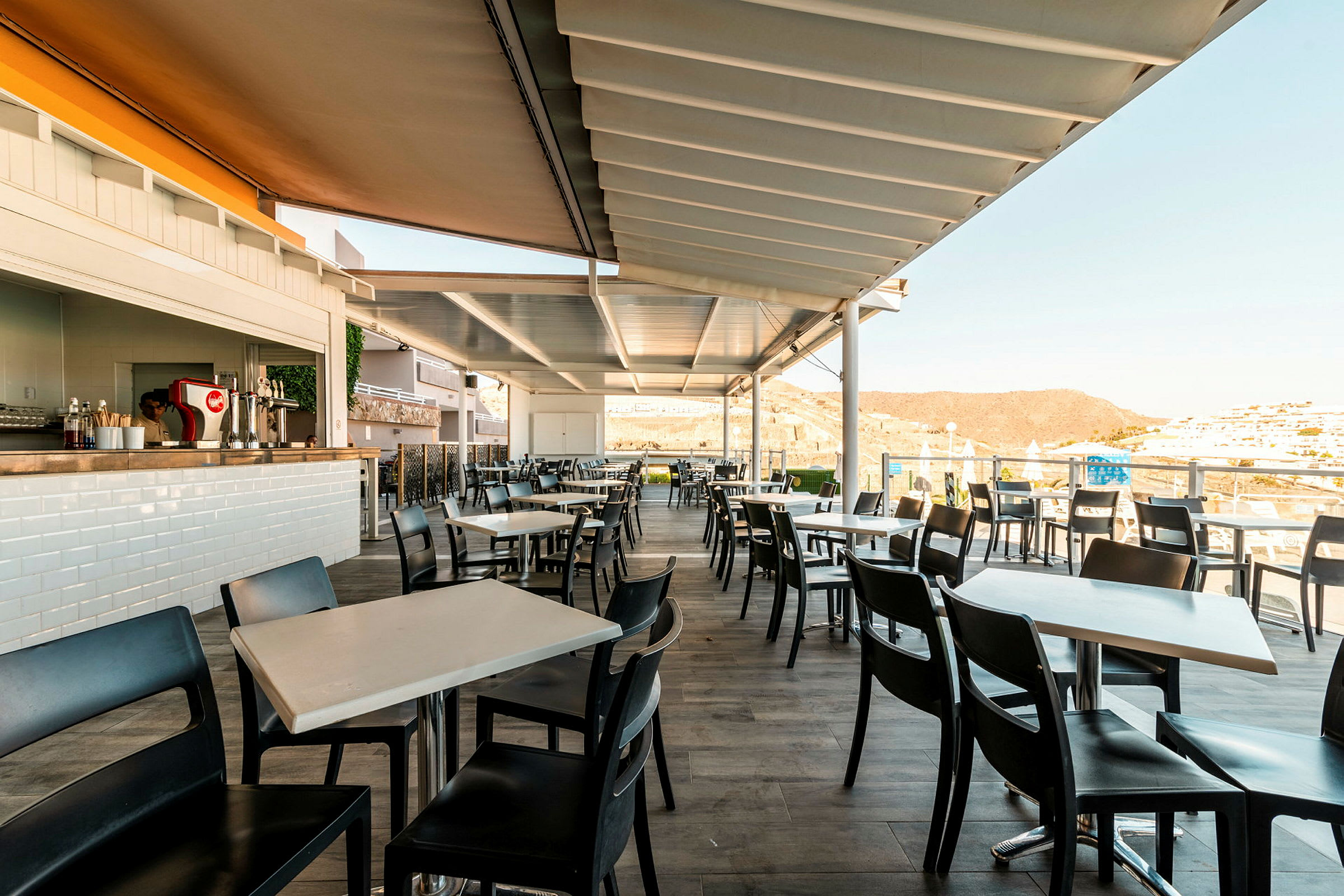 Utendørsrestaurant med moderne bord og stoler under en overbygget pergola. (AI-generert tekst)