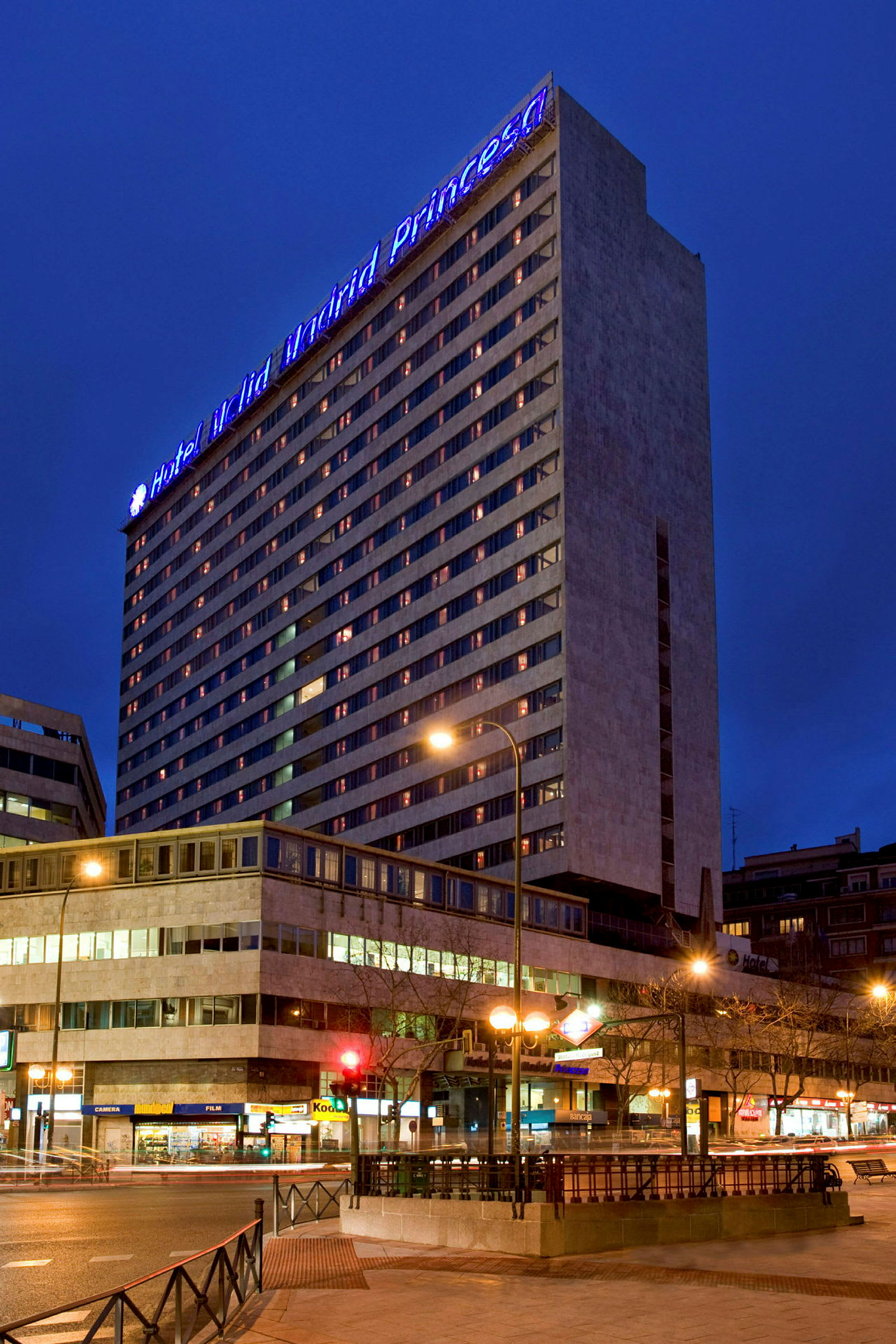 Et hotell om kvelden med opplyste vinduer og et blått skilt på toppen som lyser opp bygningen. (AI-generert tekst)