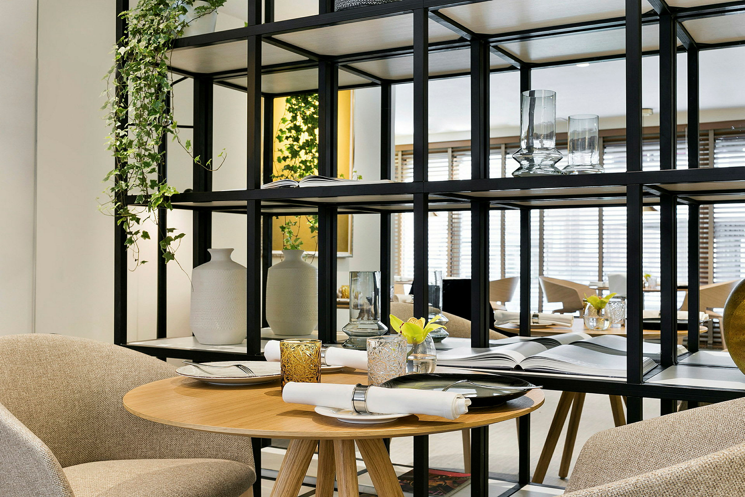 Et elegant dekket bord med serviett og glass, omgitt av dekorative hyller og planter. (AI-generert tekst)