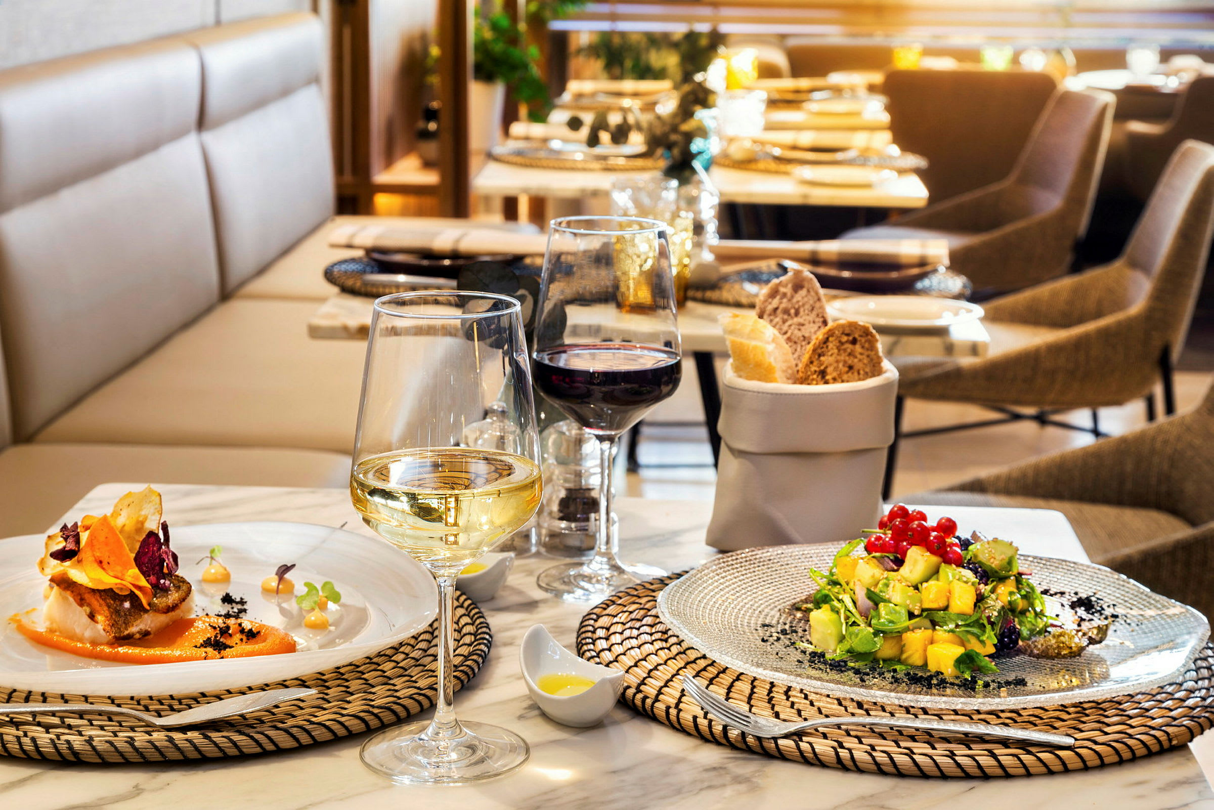 Et dekket bord på en restaurant med to tallerkener mat, vinglass og en brødkurv. (AI-generert tekst)
