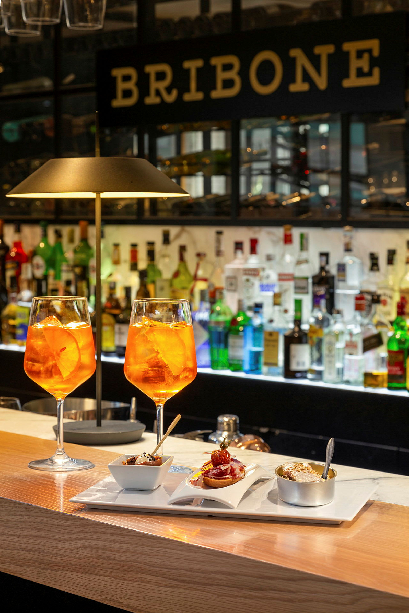 To glass med oransje drikke og en tallerken med forskjellige småretter står på en bardisk. (AI-generert tekst)
