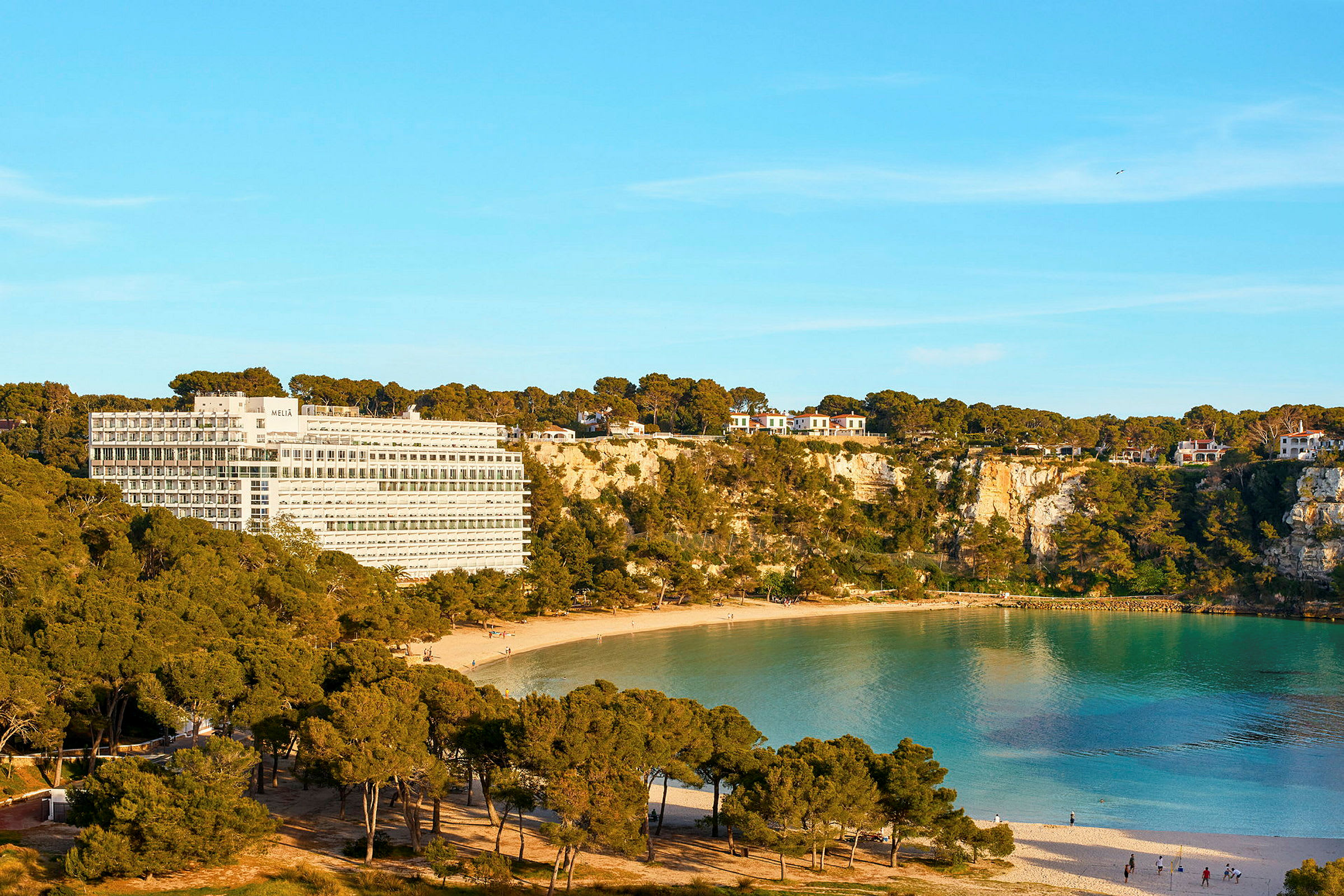 Hotellbygning ved en klippekyst med en sandstrand og turkist vann. (AI-generert tekst)