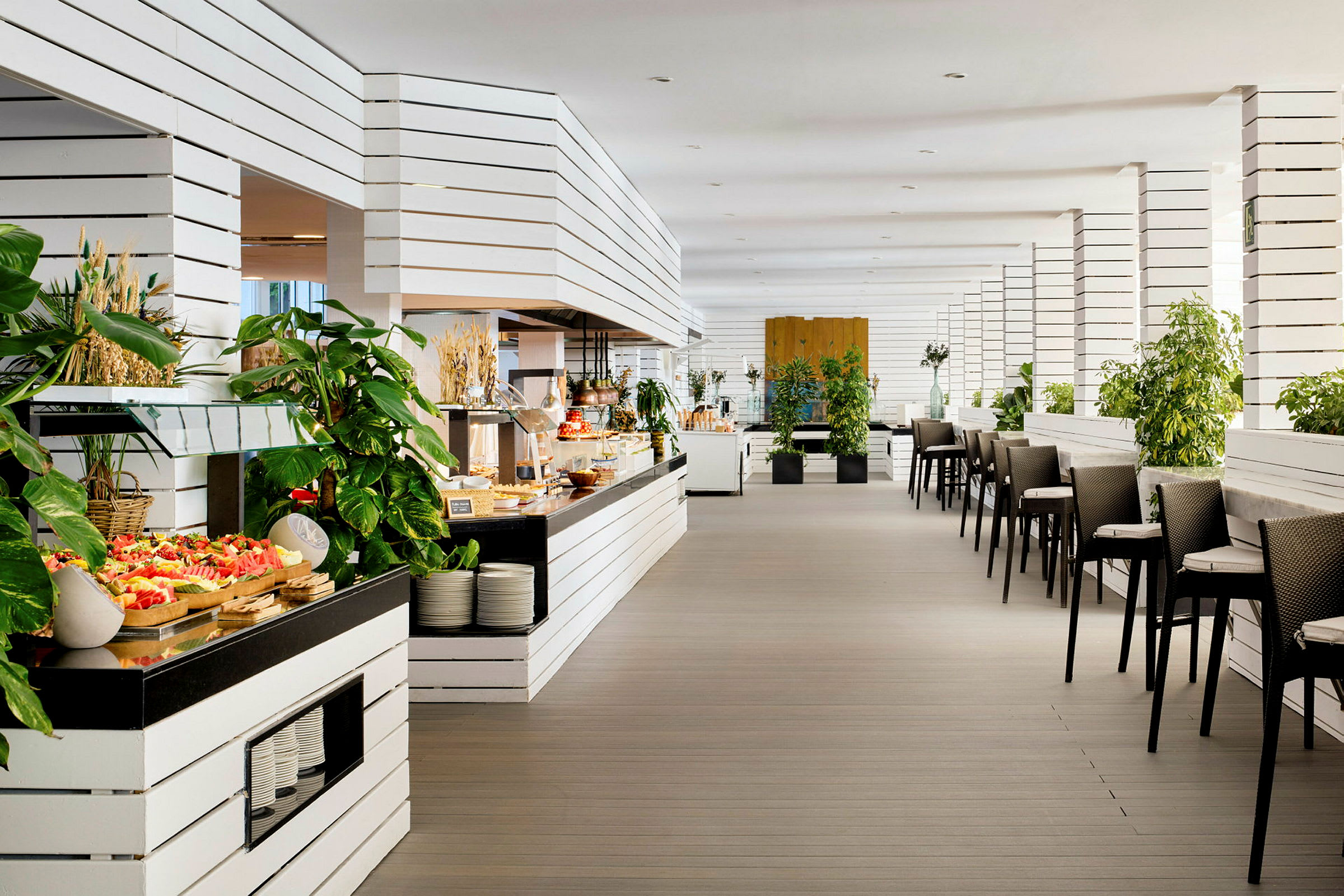 Innredning av en moderne restaurant med hvite trepaneler, grønne planter og serveringsbord fylt med mat. (AI-generert tekst)