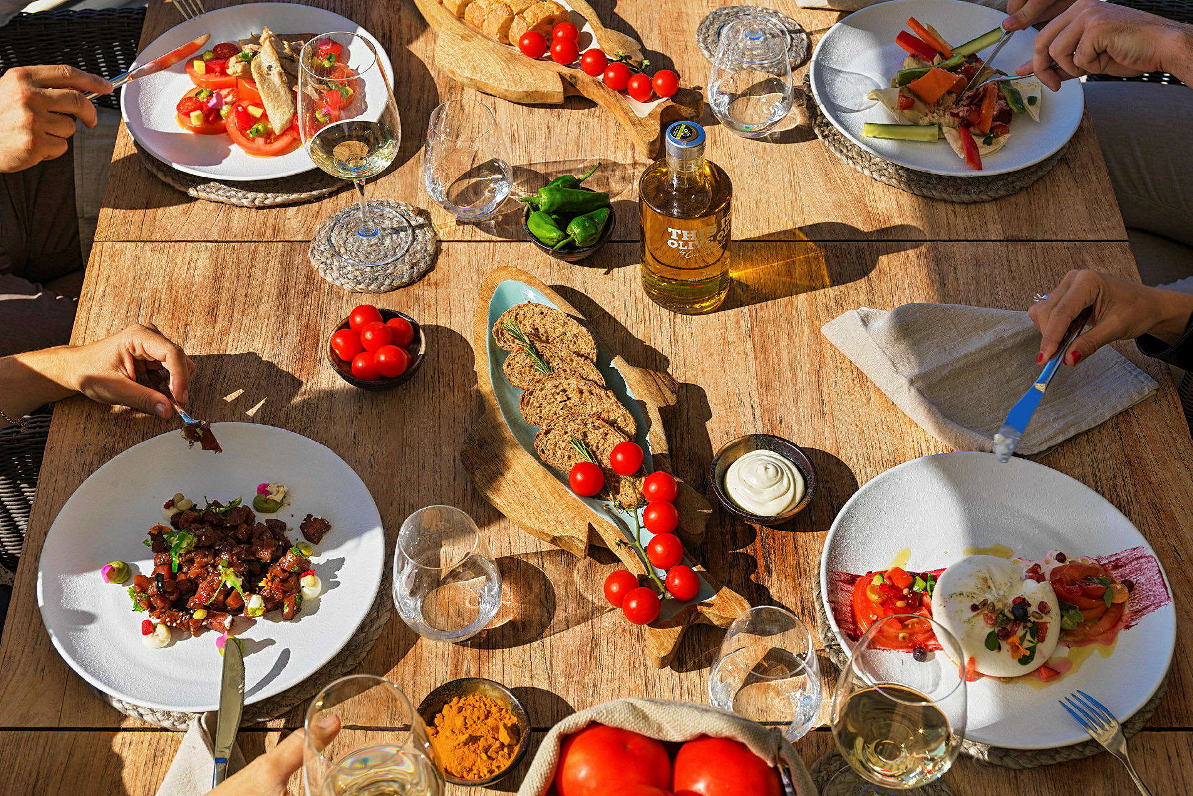 Et bord dekket med tallerkener fylt med salat og andre retter, omgitt av glass og skåler med olje, brød og tilbehør. (AI-generert tekst)