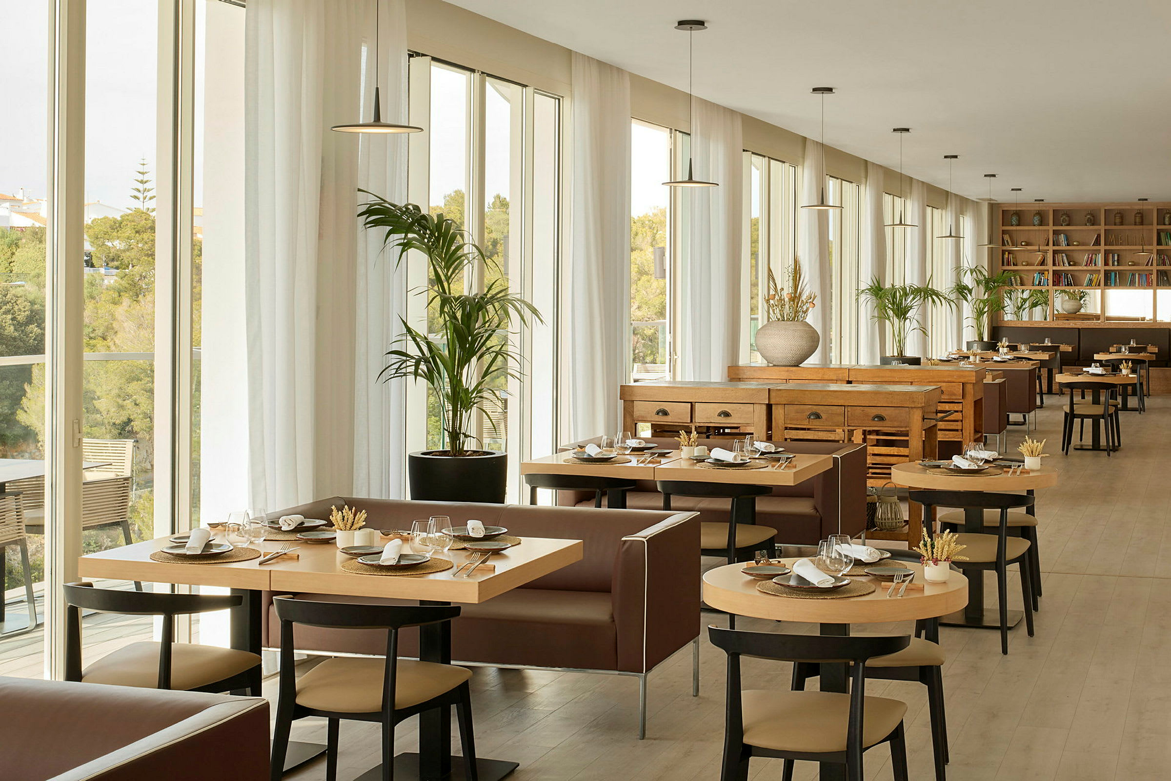 En lys og romslig restaurant med store vinduer, moderne møbler og bord dekket til måltider. (AI-generert tekst)