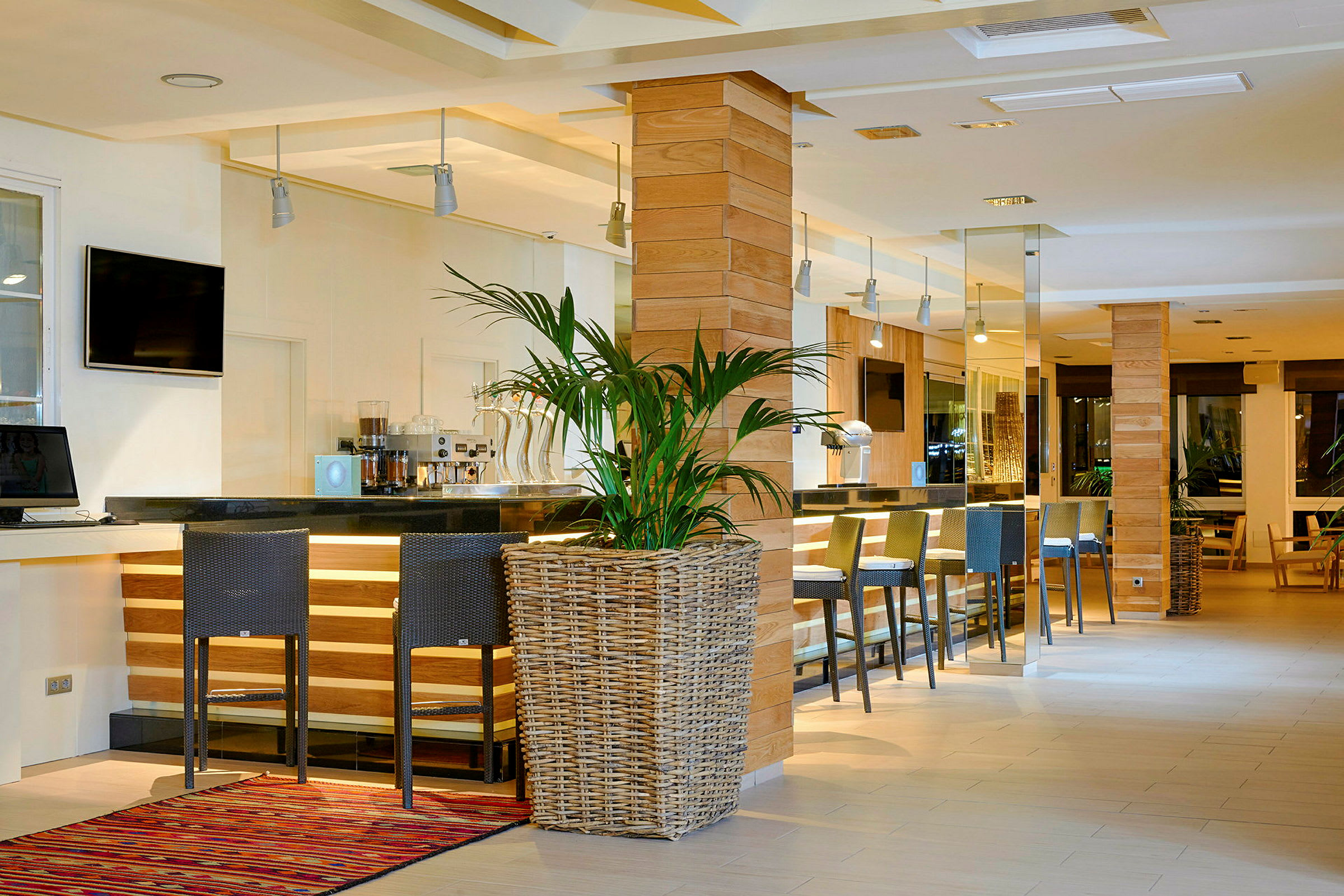 Bilde av en moderne og stilfull hotellbar med høye stoler, en bardisk i svart, trepaneler og en stor potteplante i forgrunnen. (AI-generert tekst)